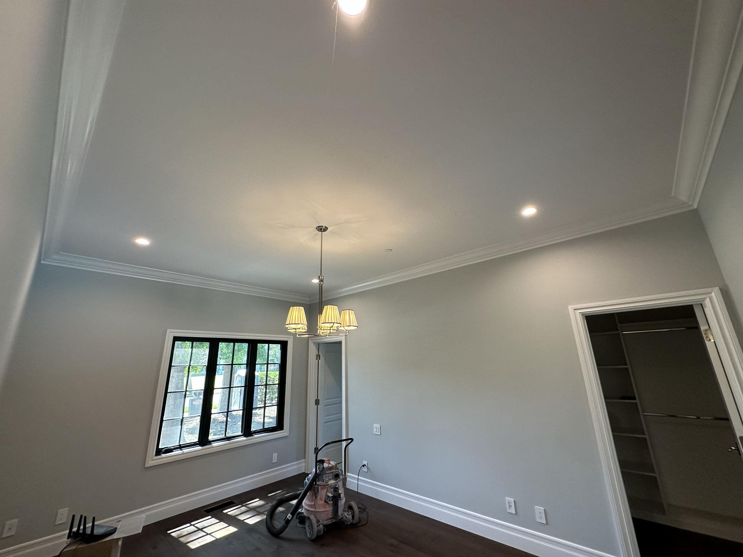Empty living room with light-colored walls, a window with black frames, a ceiling light fixture, and a floor cleaning machine in the center.