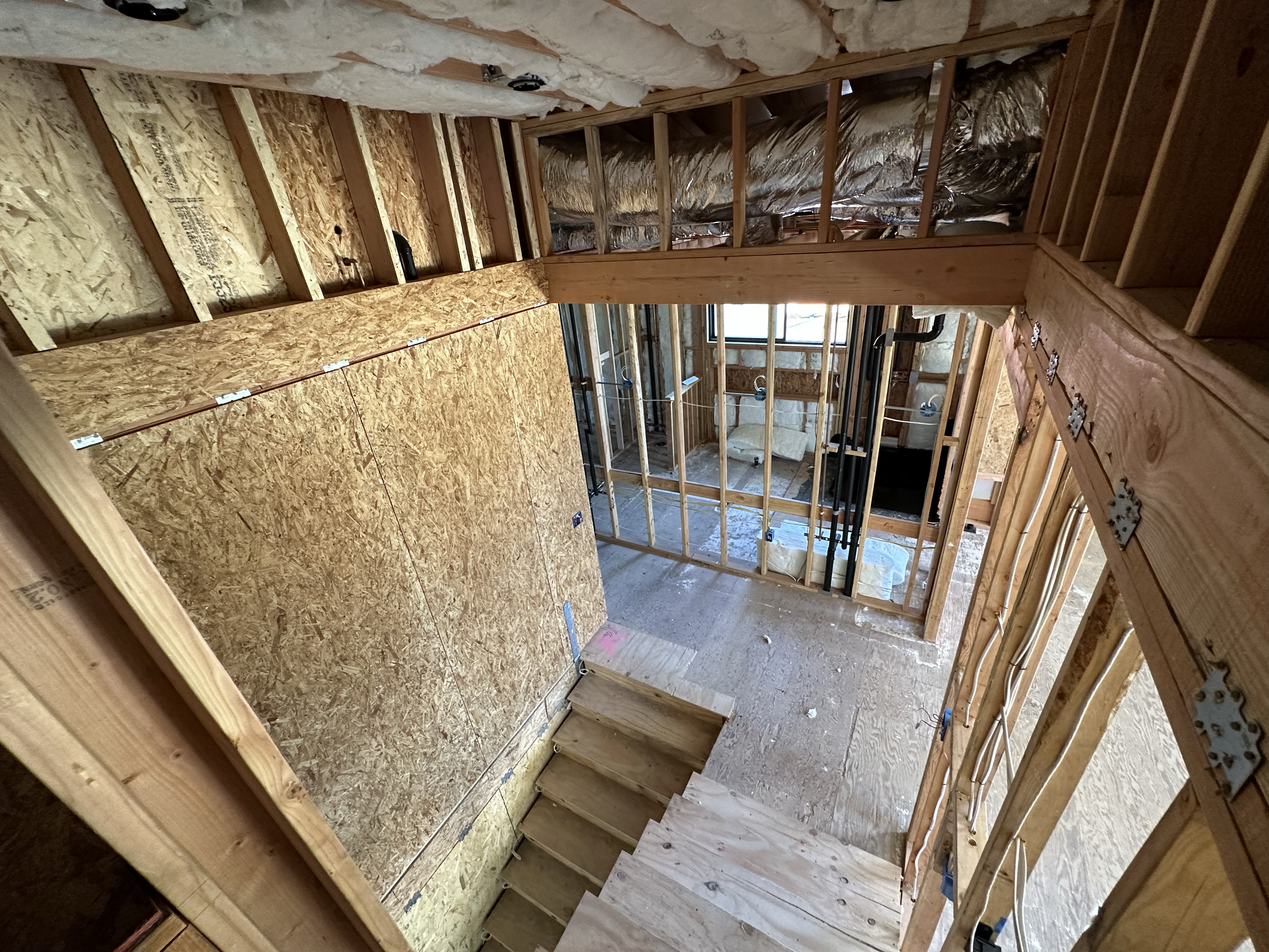 This image shows the interior of a building under construction, with exposed wooden framing, electrical wiring, and insulation in the walls and ceiling.