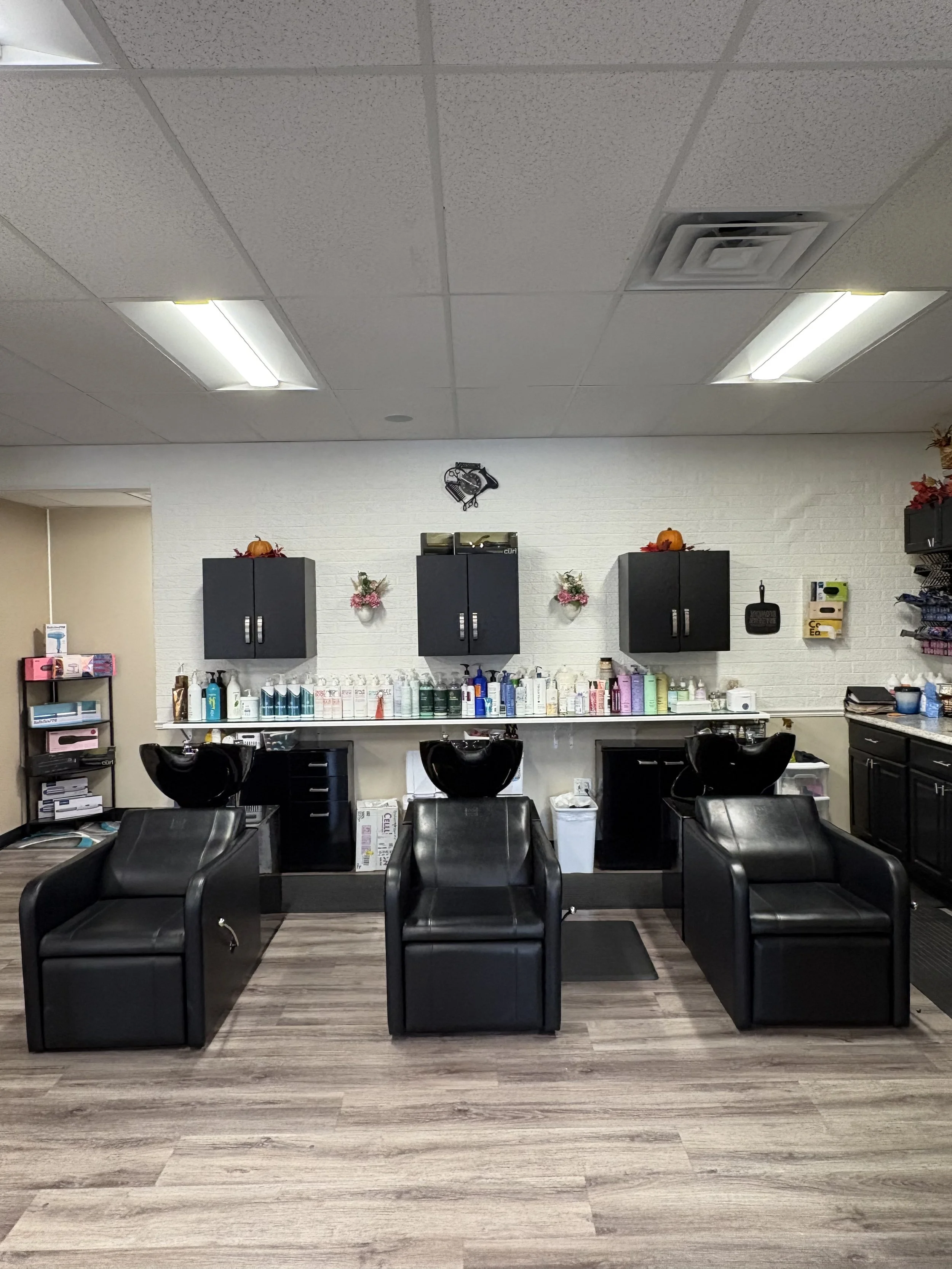3 Salon wash bowls facing a wall with black cabinets, decorations, and hair care products.