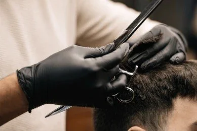 A barber wearing black gloves is cutting a person's hair with scissors.