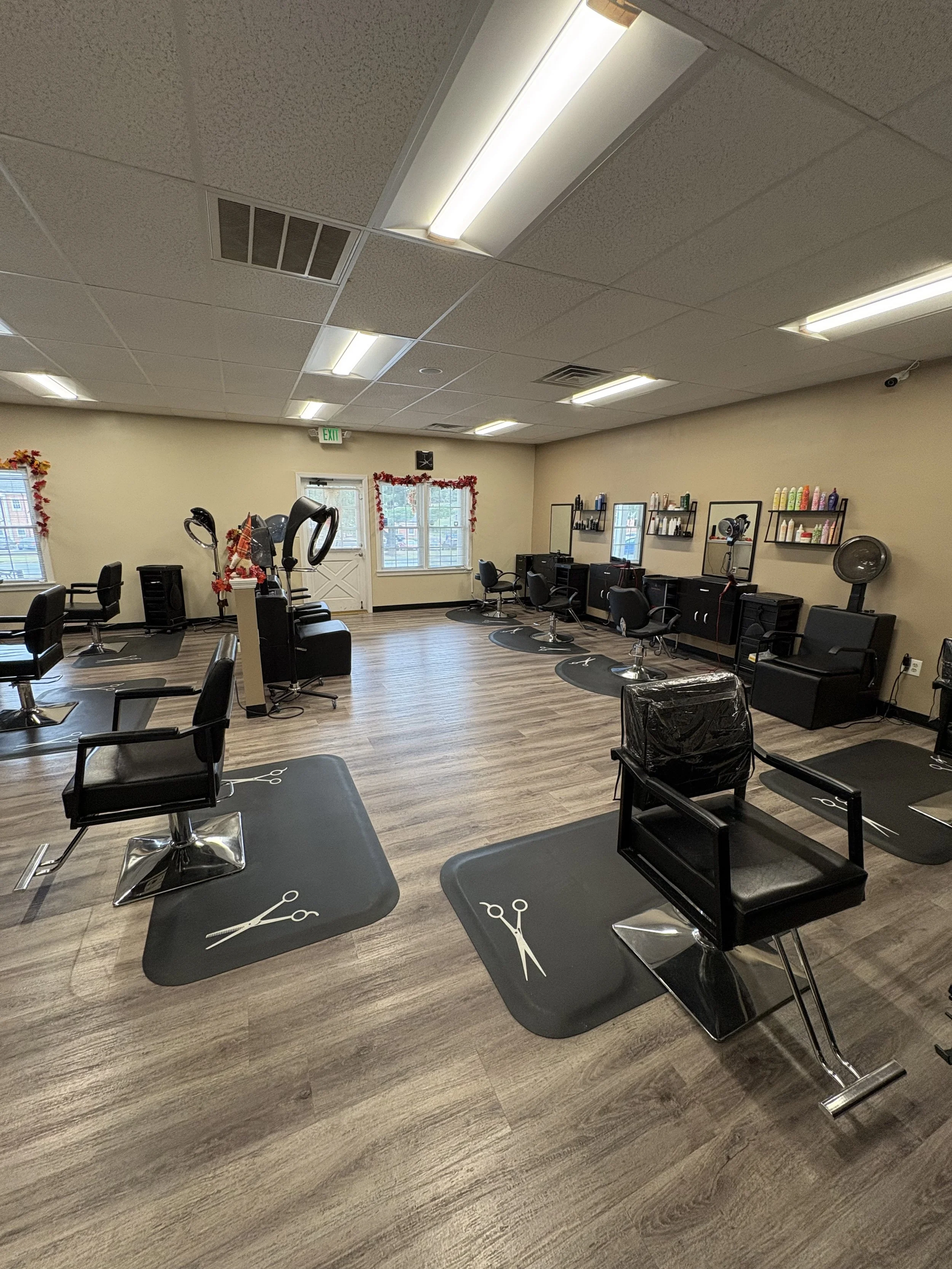A hair salon with multiple styling chairs and workstations, mirrors, shelves with hair products, and hair dryers, decorated with small holiday ornaments and a wooden floor.