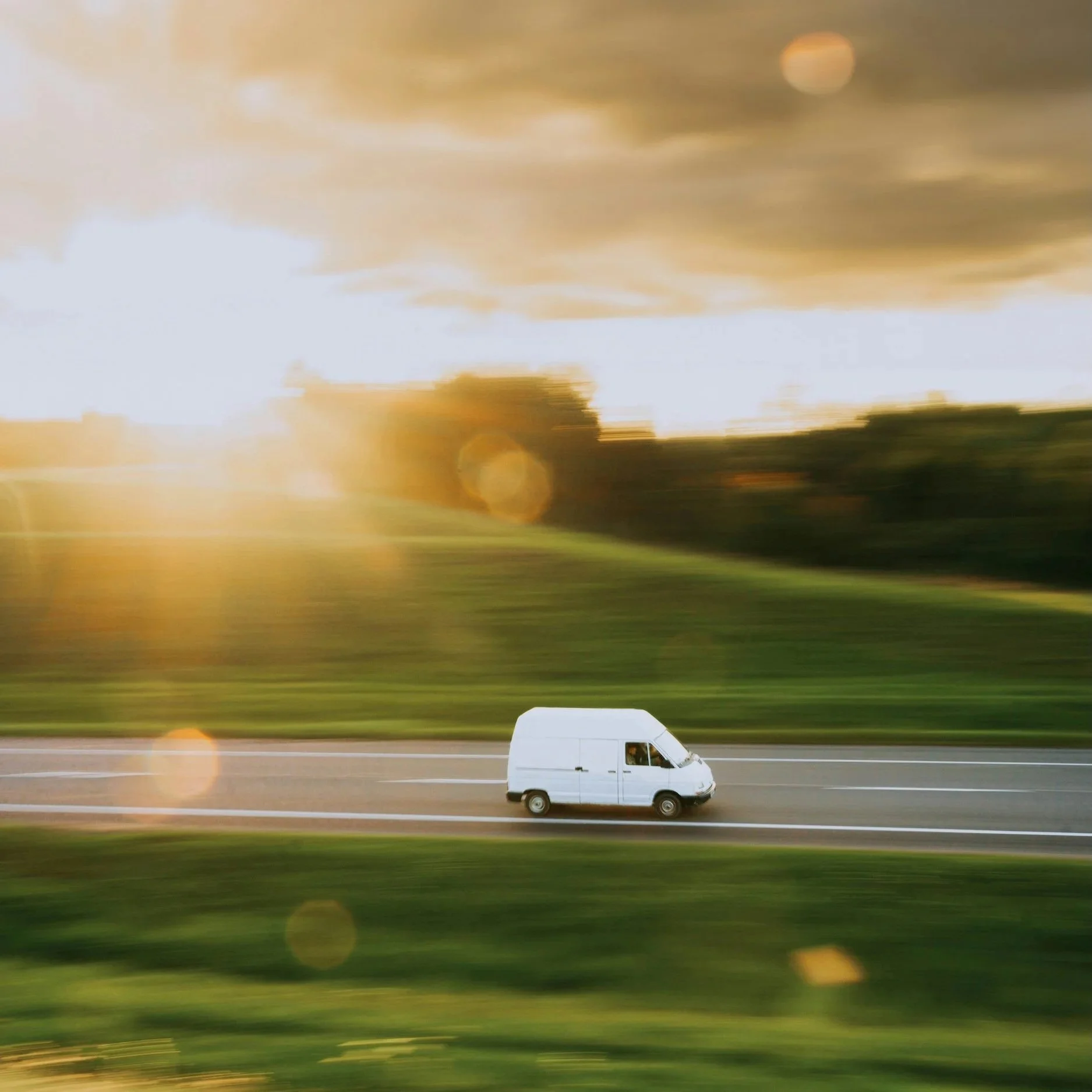 Photo of a Delivery Van Driving Down a Road at Sunrise
