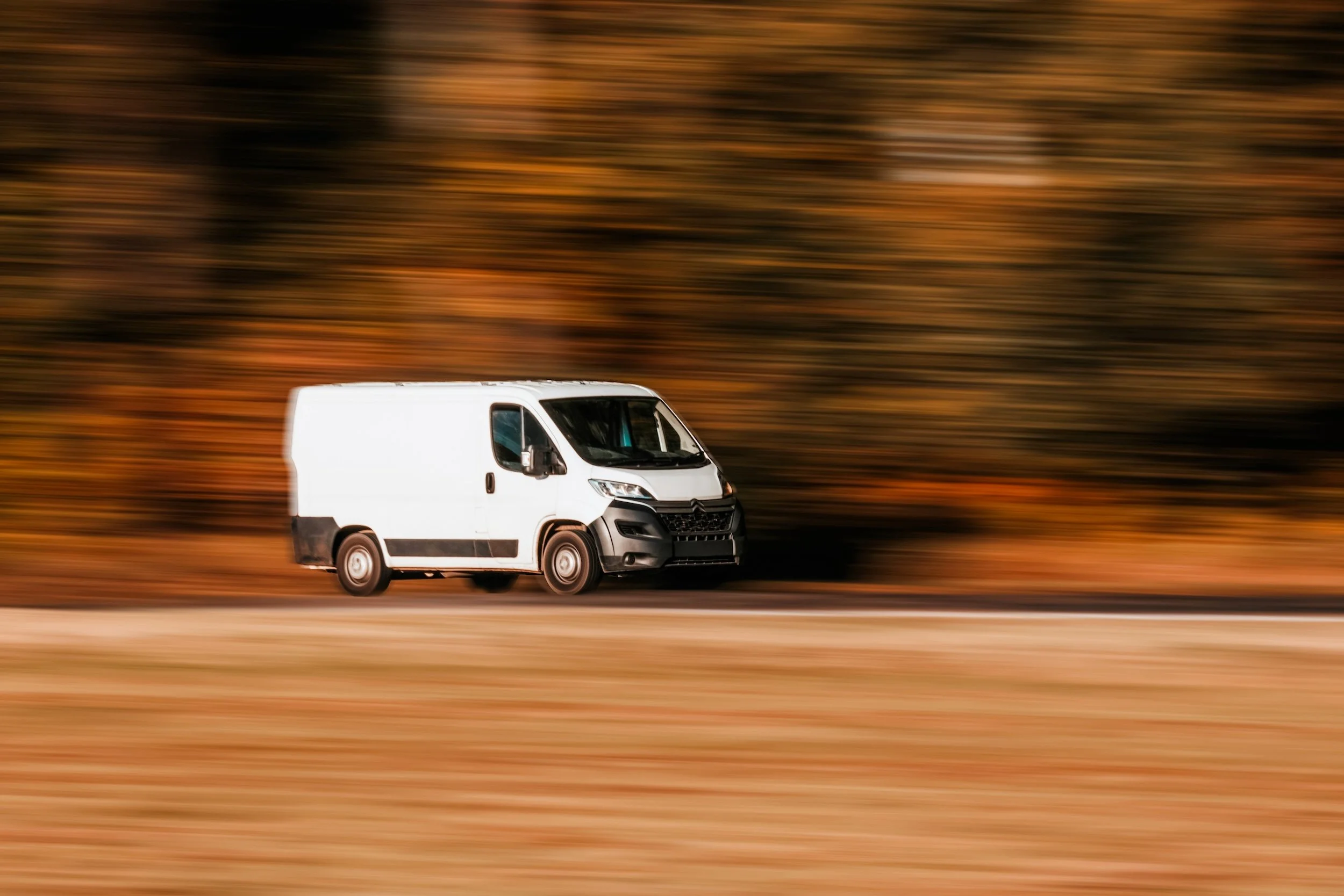 Photo of a White Delivery Van Driving Down an Autumn Road