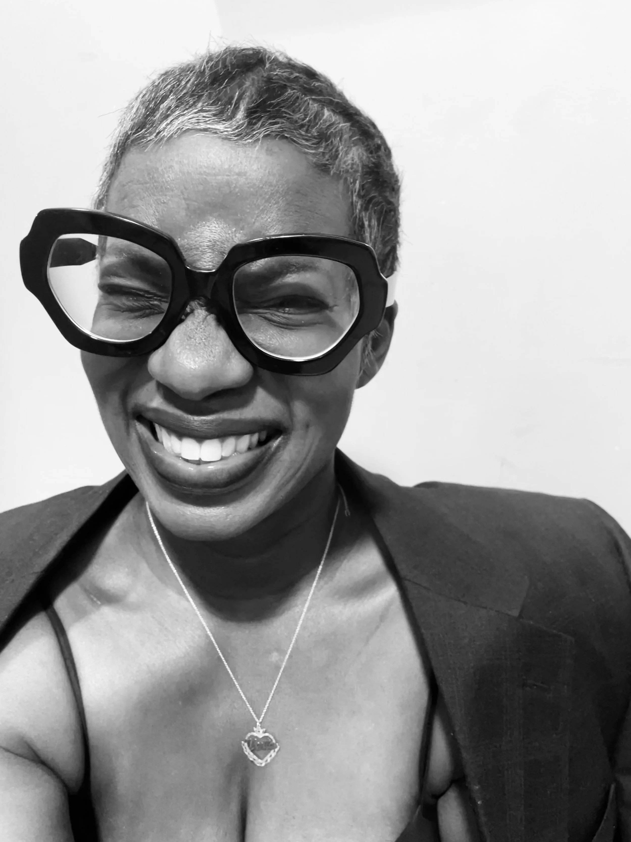 Black-and-white portrait of Verta Maloney, co-founder of 45 Lemons, smiling, wearing glasses, a necklace with a heart-shaped pendant, and a top with thin straps.