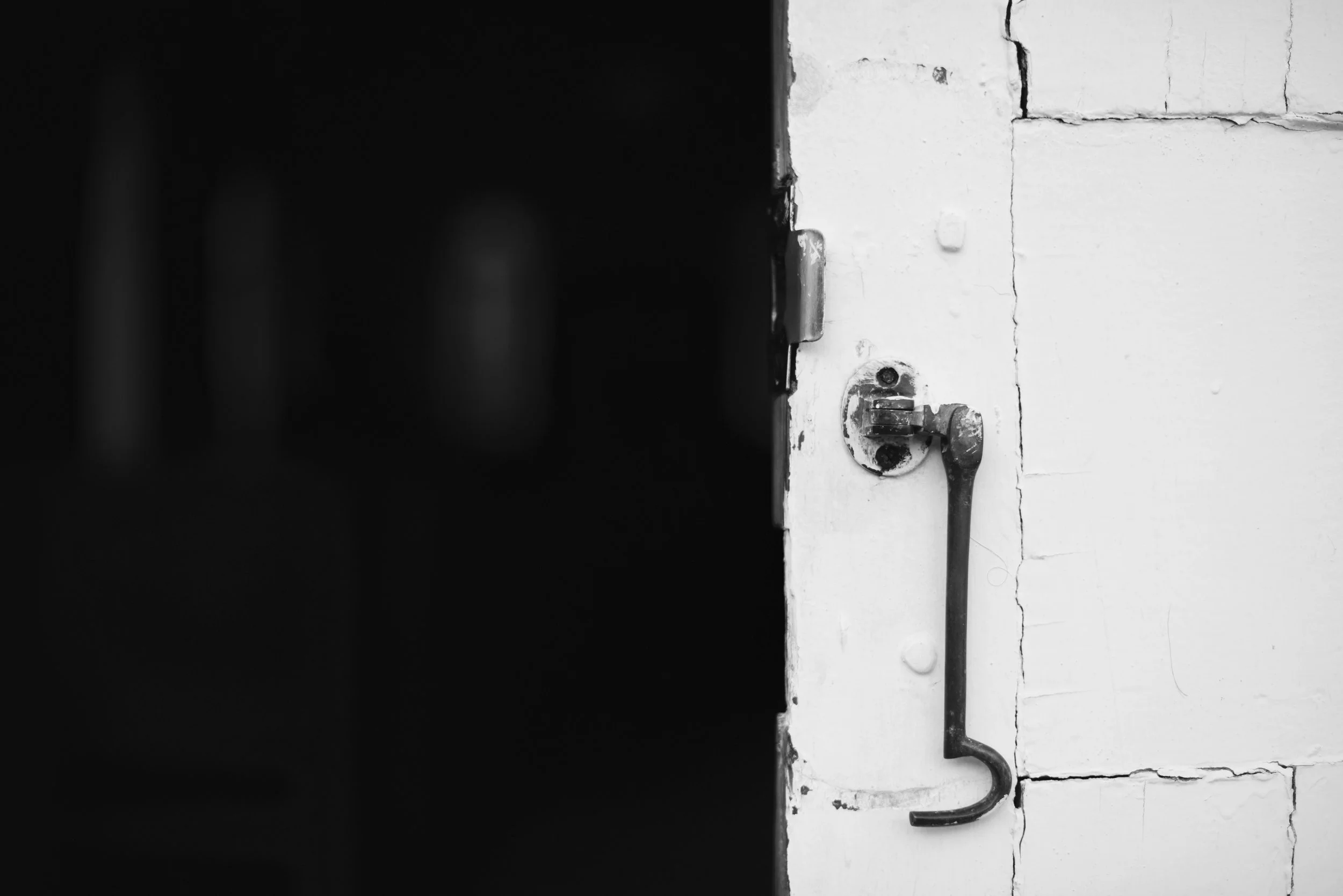 Close-up of a door latch and handle on a white brick wall, with a dark shadowy area on the left.