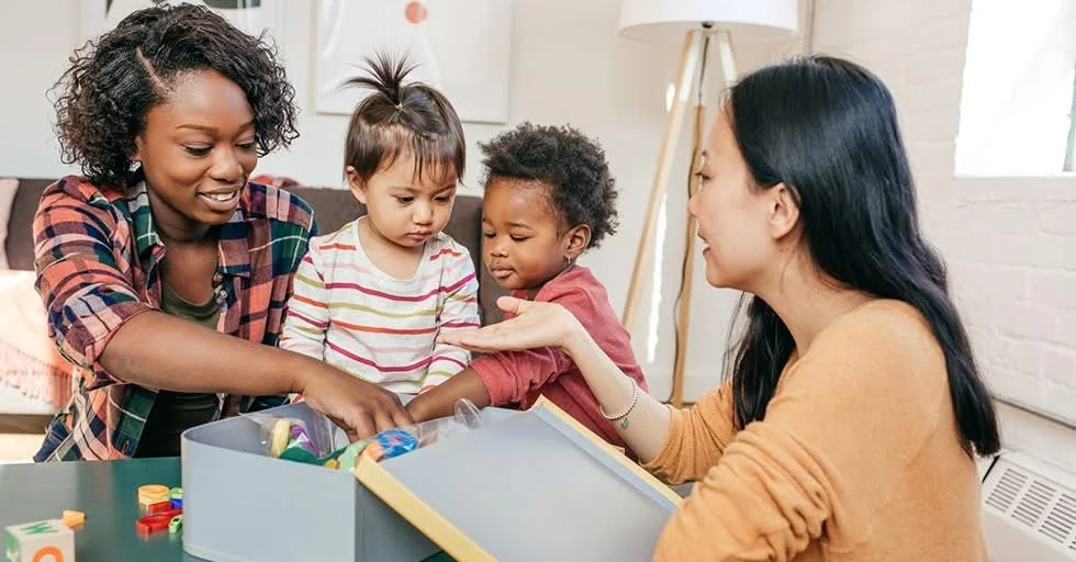 Two women and two children at a table opening a box of colorful toys