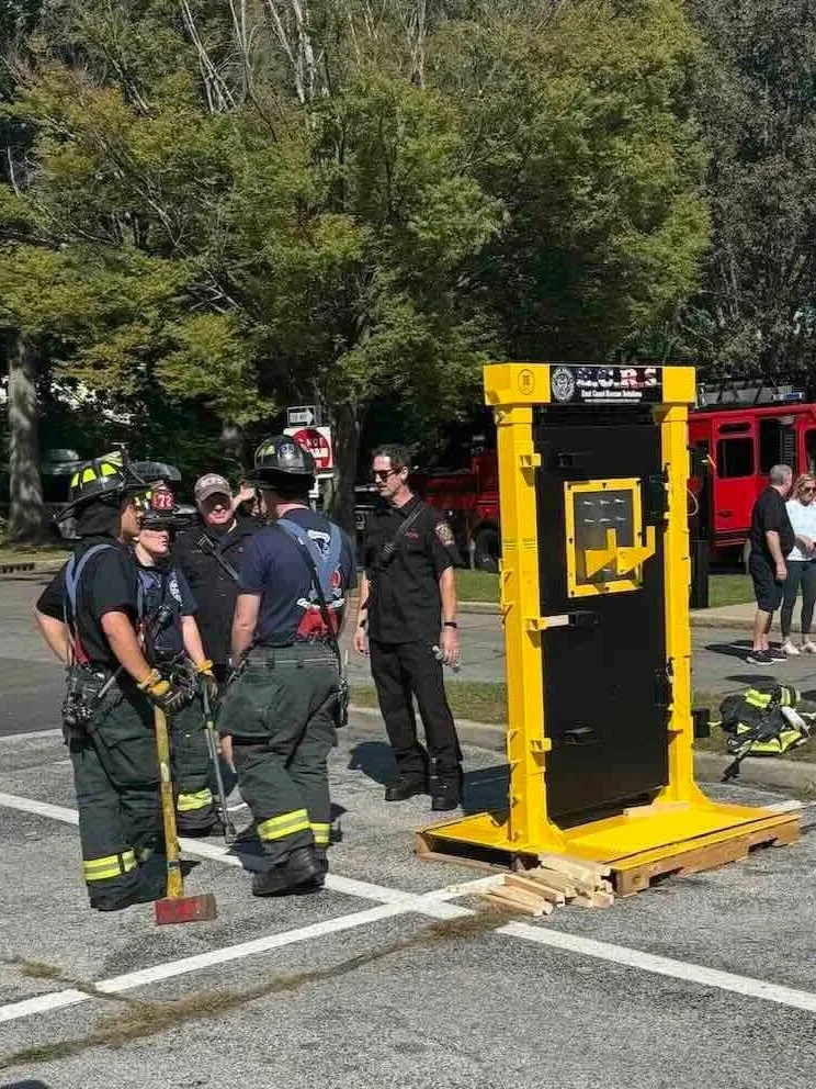 A group of Garden City firefighters and a police officer standing in a parking lot near the reinforced door supplied for training by Council l1869 to help firefighters better prepare for real world scenarios