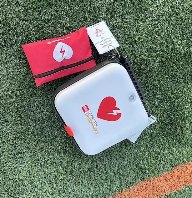 Automated external defibrillator (AED) device on grassy field with red and black pouch attached