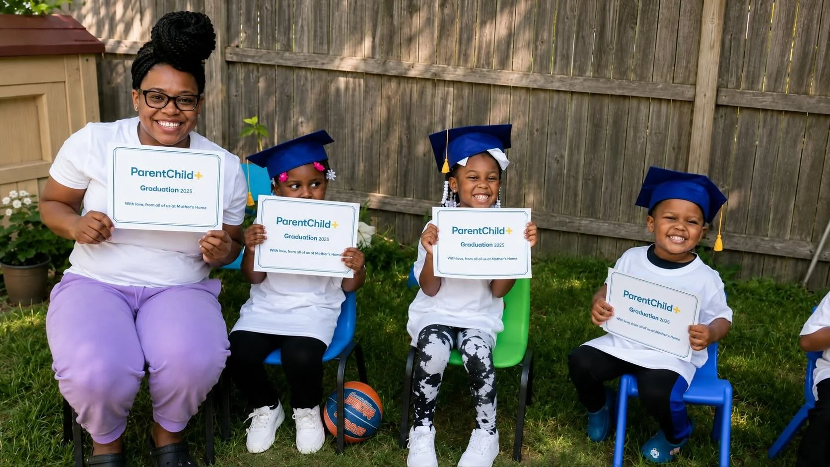 A smiling woman and four young children sitting outside on chairs, celebrating graduation with certificates. The children are wearing blue caps and white shirts, holding up signs that read "ParentChild+ Graduation 2025." The setting appears to be a backyard with a wooden fence and grass.