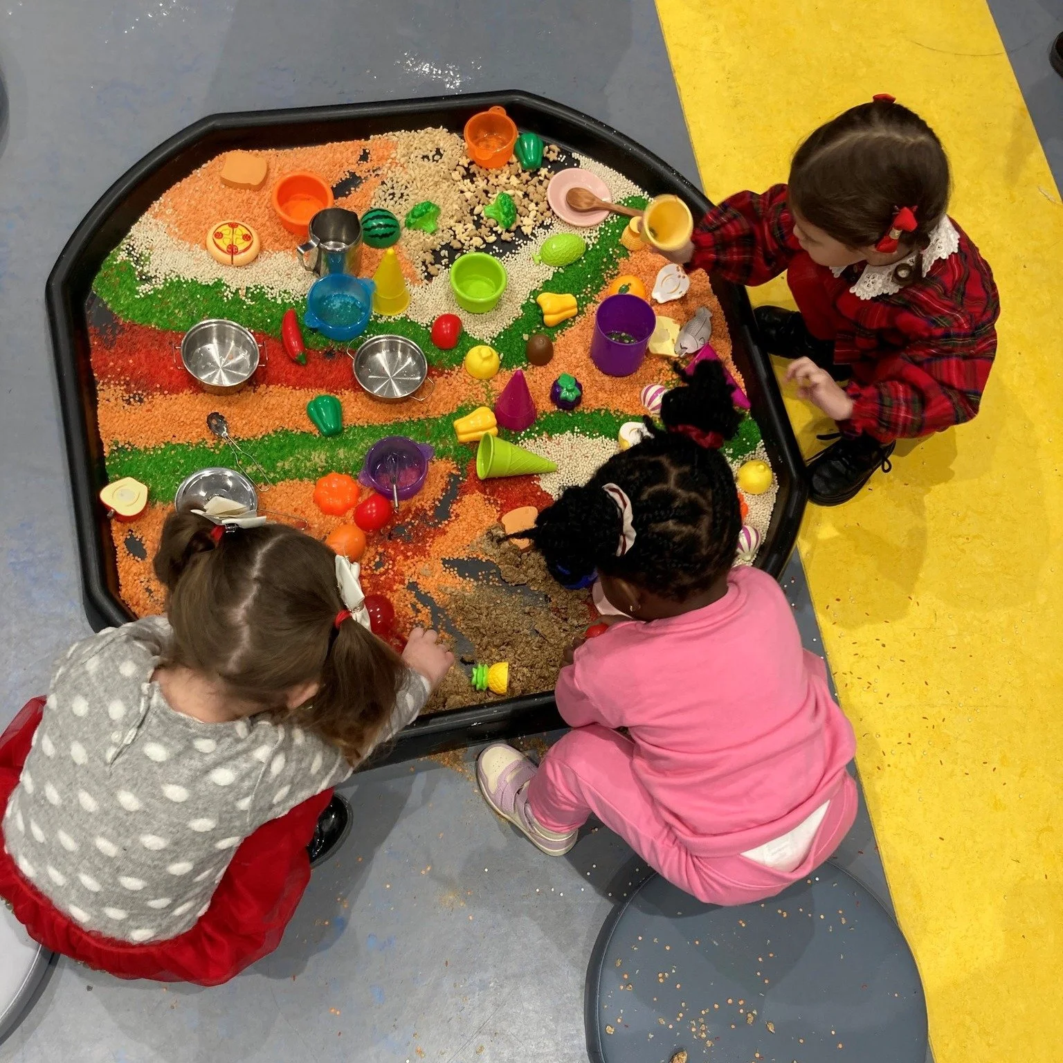 Children playing in a sensory exhibit with colored rice, plastic toys, and bowls.