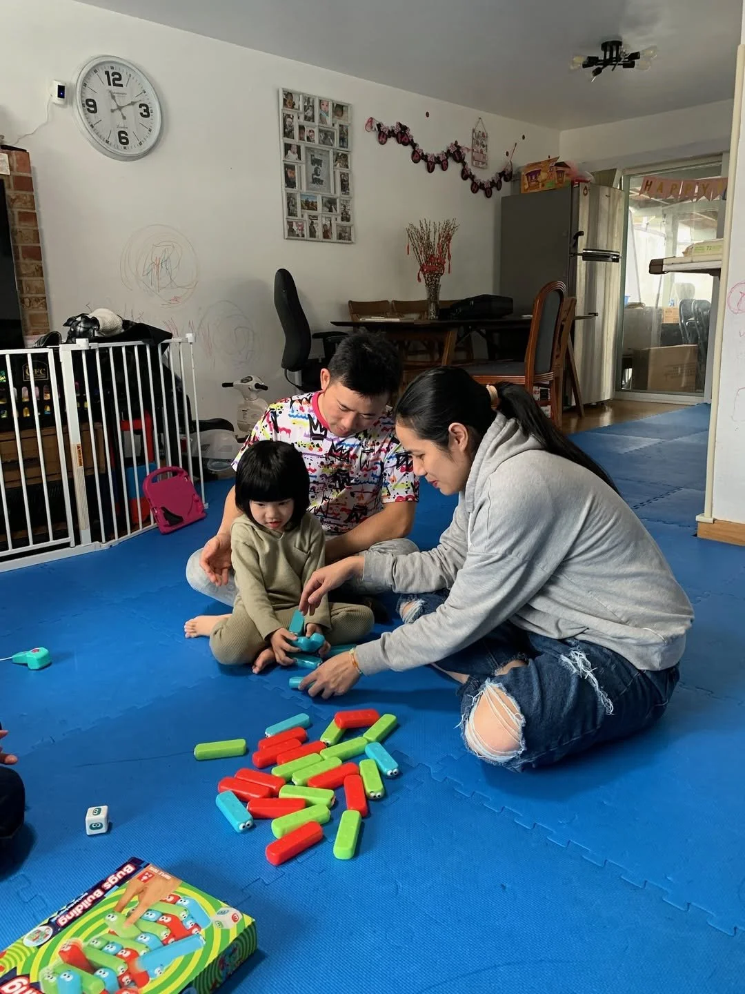 A family playing the game 'Bus Stop' with colorful pieces on a blue mat in a living room.