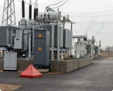 Electrical transformers and equipment at a power substation with overcast skies and power lines.