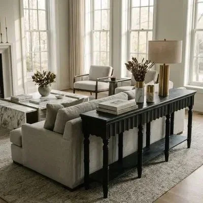 Living room with beige sofa, two armchairs, large windows, black console table with decorative items, and a lamp.