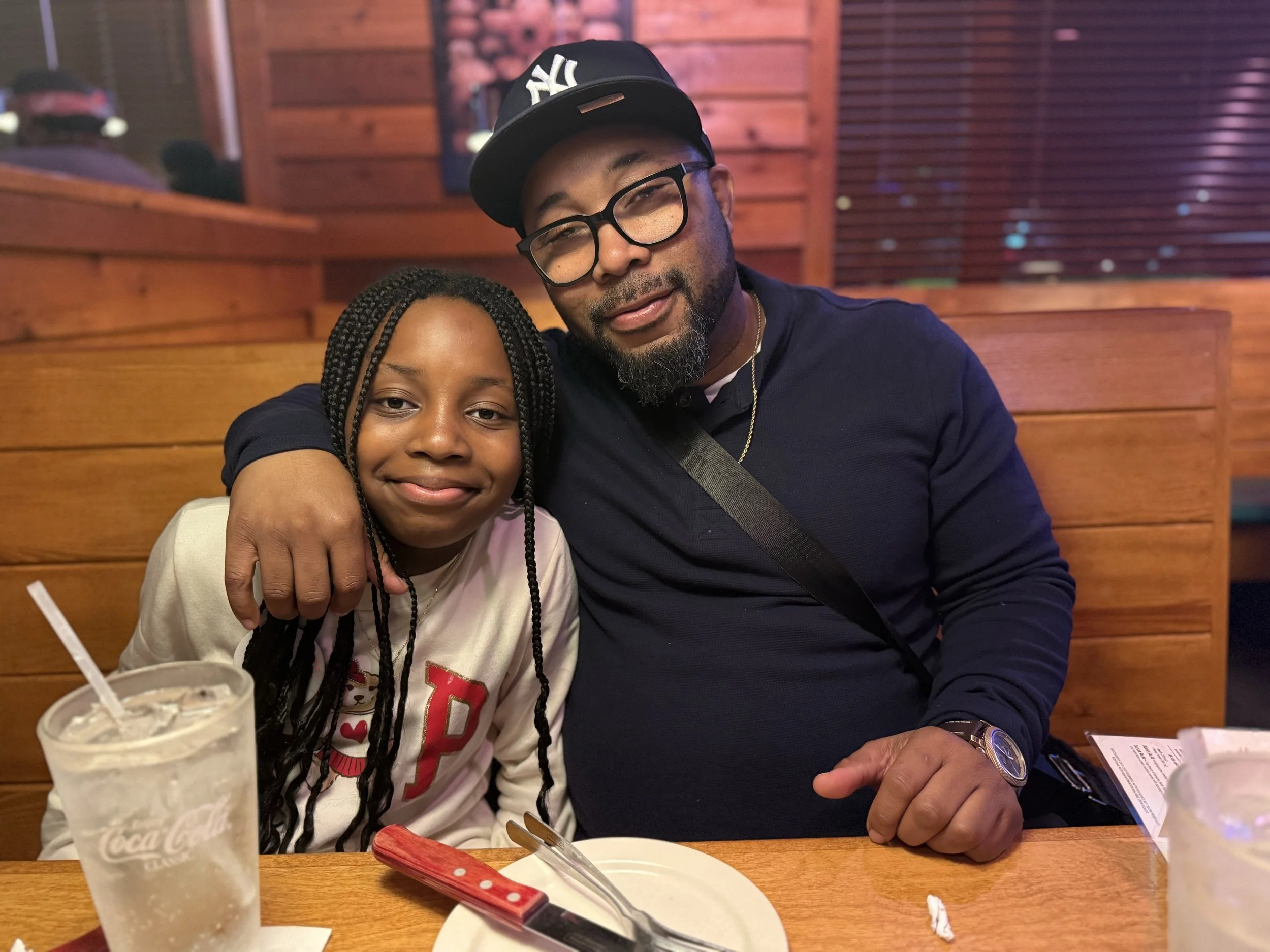 A man and young girl sitting together in a restaurant, smiling, with drinks and utensils on the table.