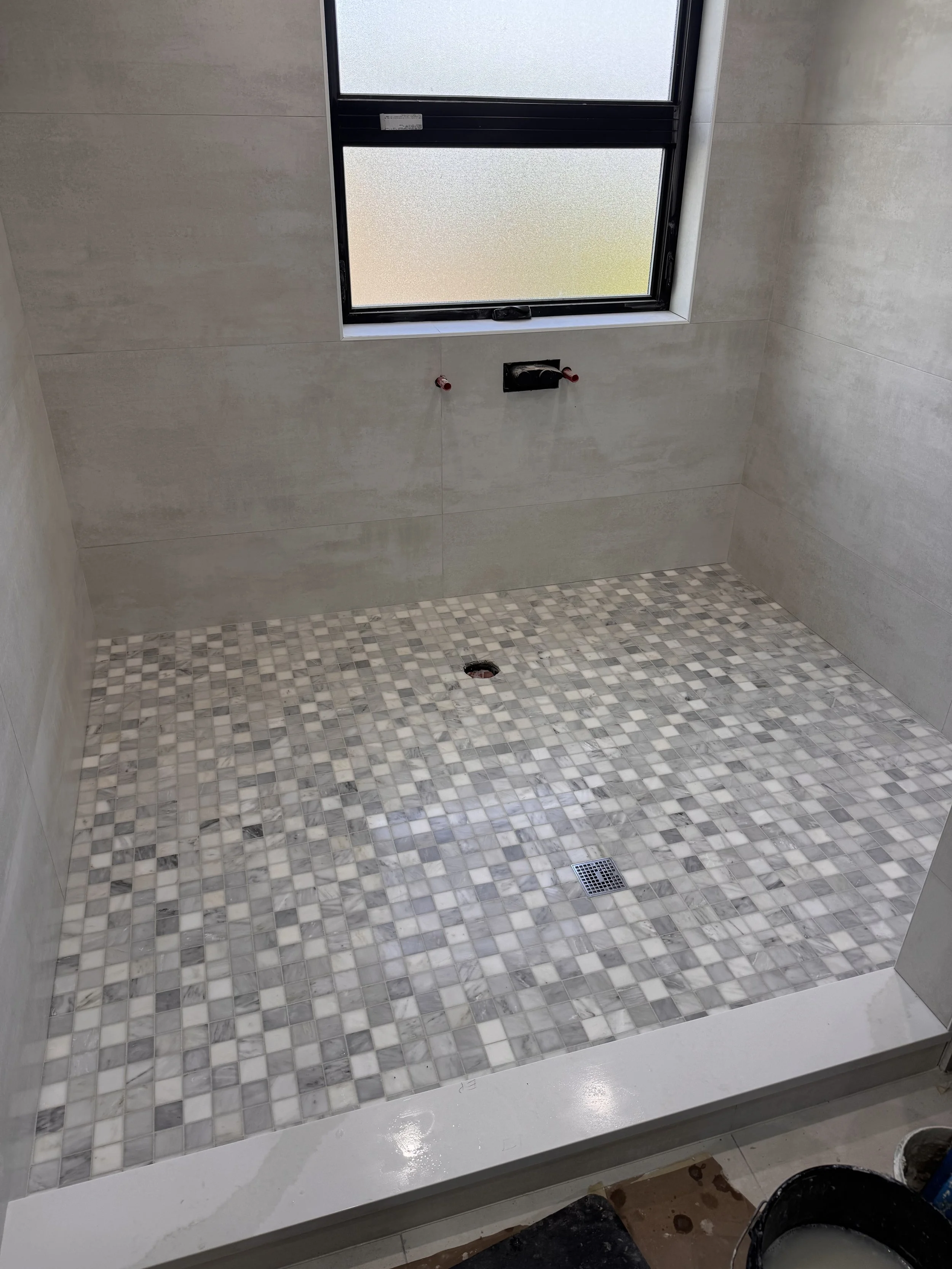 Tile floor and wall with window, no fixtures installed, construction materials and tools present