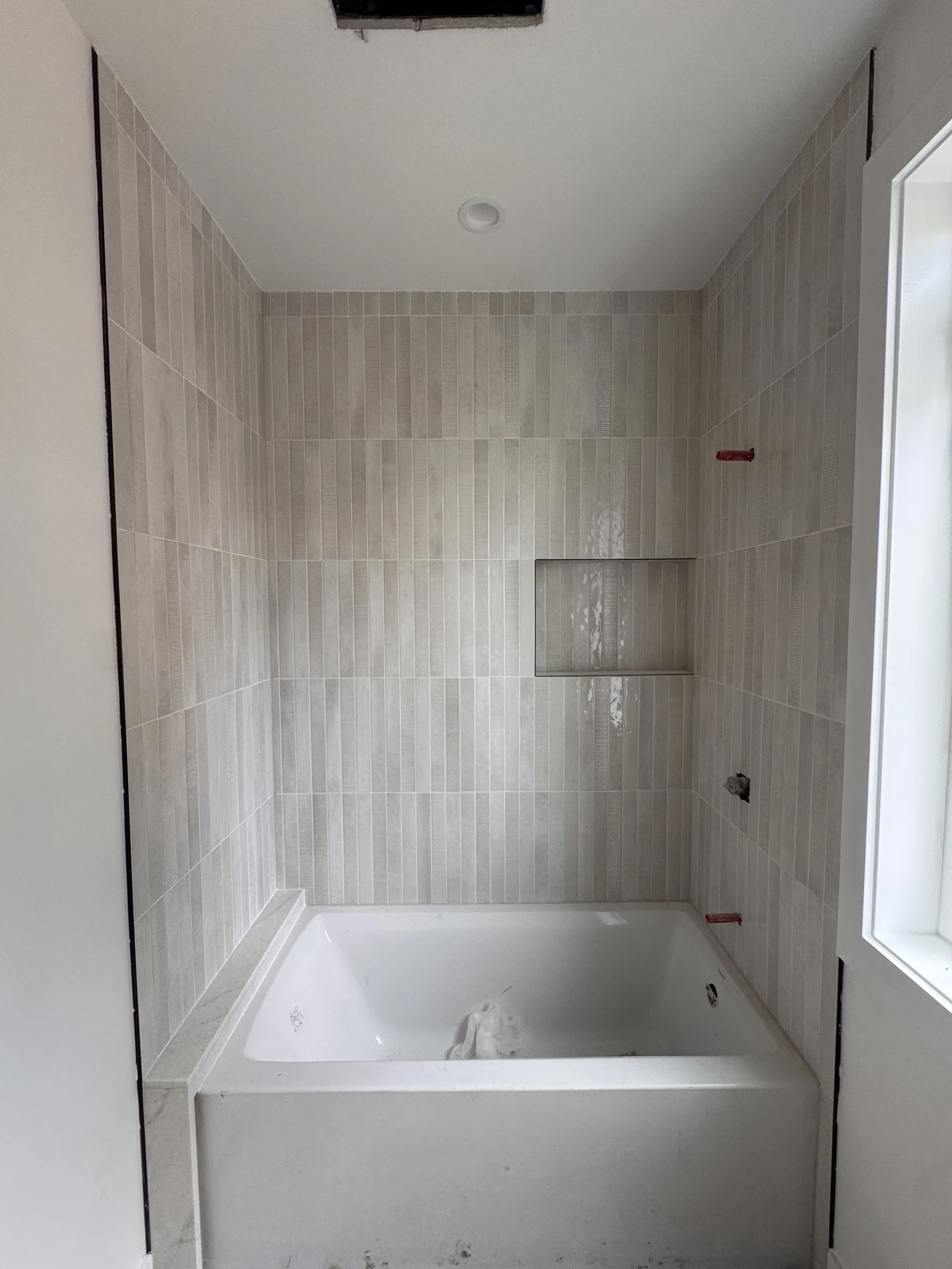Bathroom under construction with a bathtub, beige tiled walls, unfinished walls, and a ceiling vent.