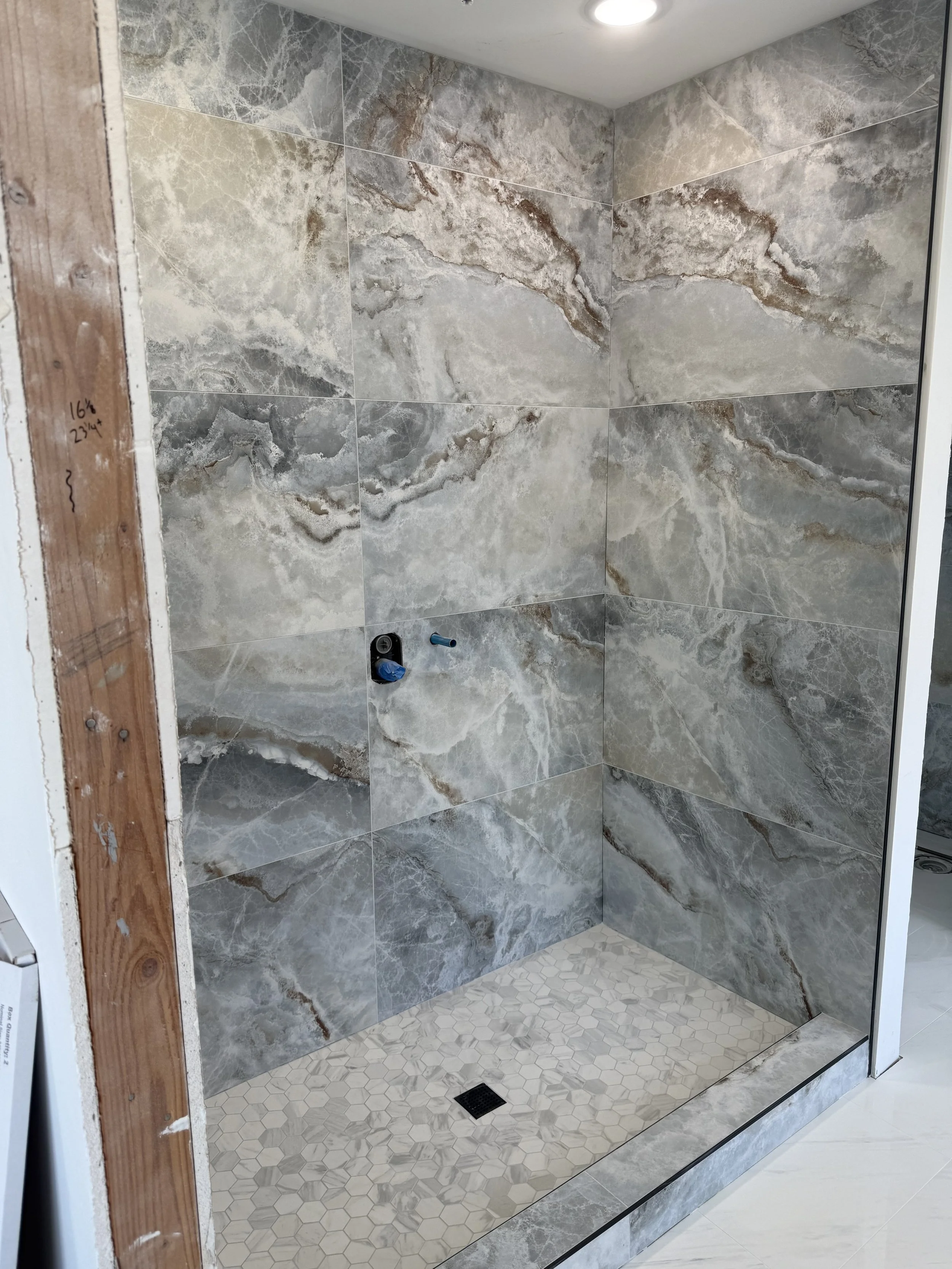 A modern shower area with marble-patterned tiles on the walls and small hexagonal tiles on the shower floor with a drain.