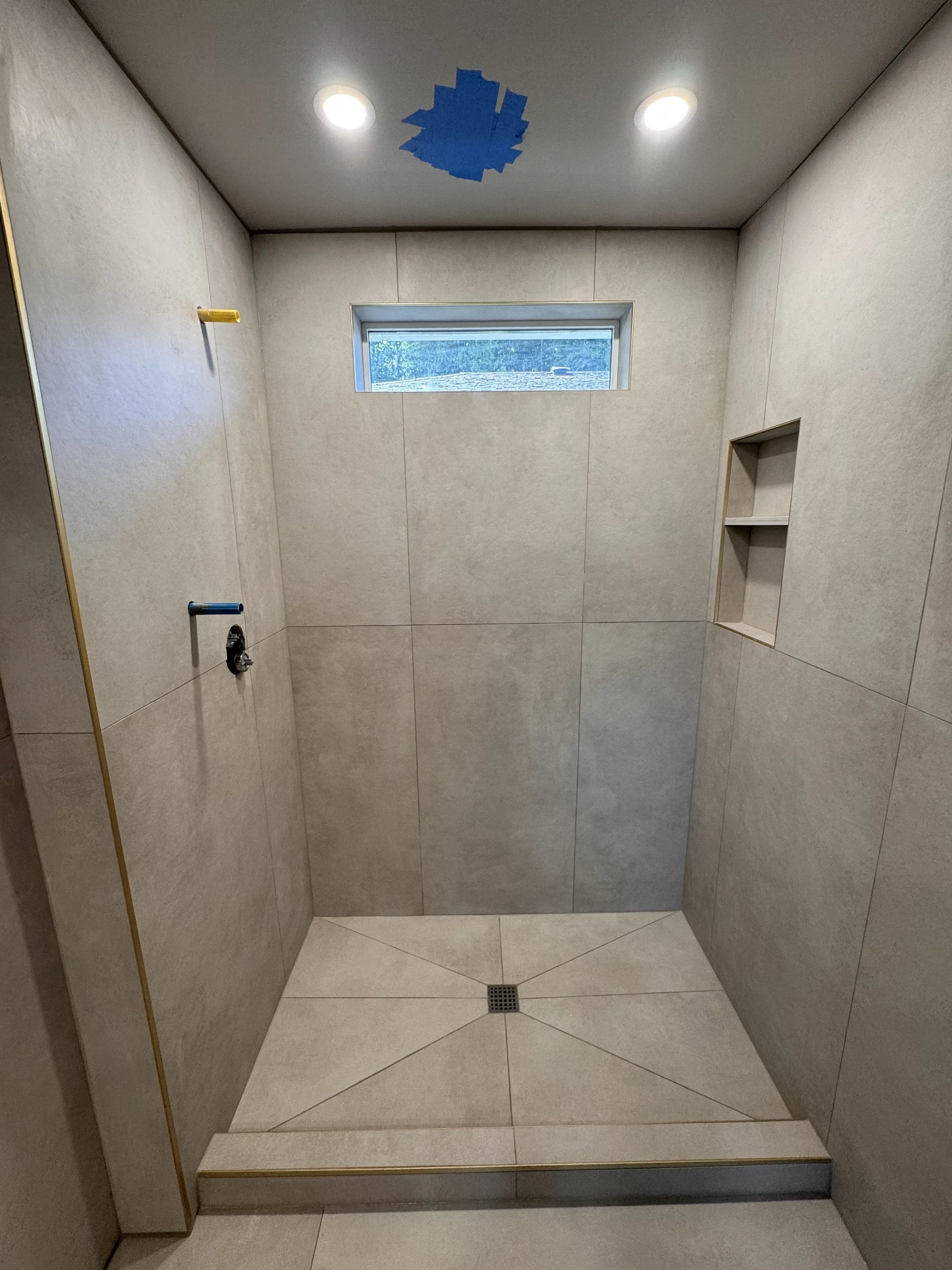 Empty shower with beige tiles, built-in niche, small window, two recessed lights, and a floor drain.