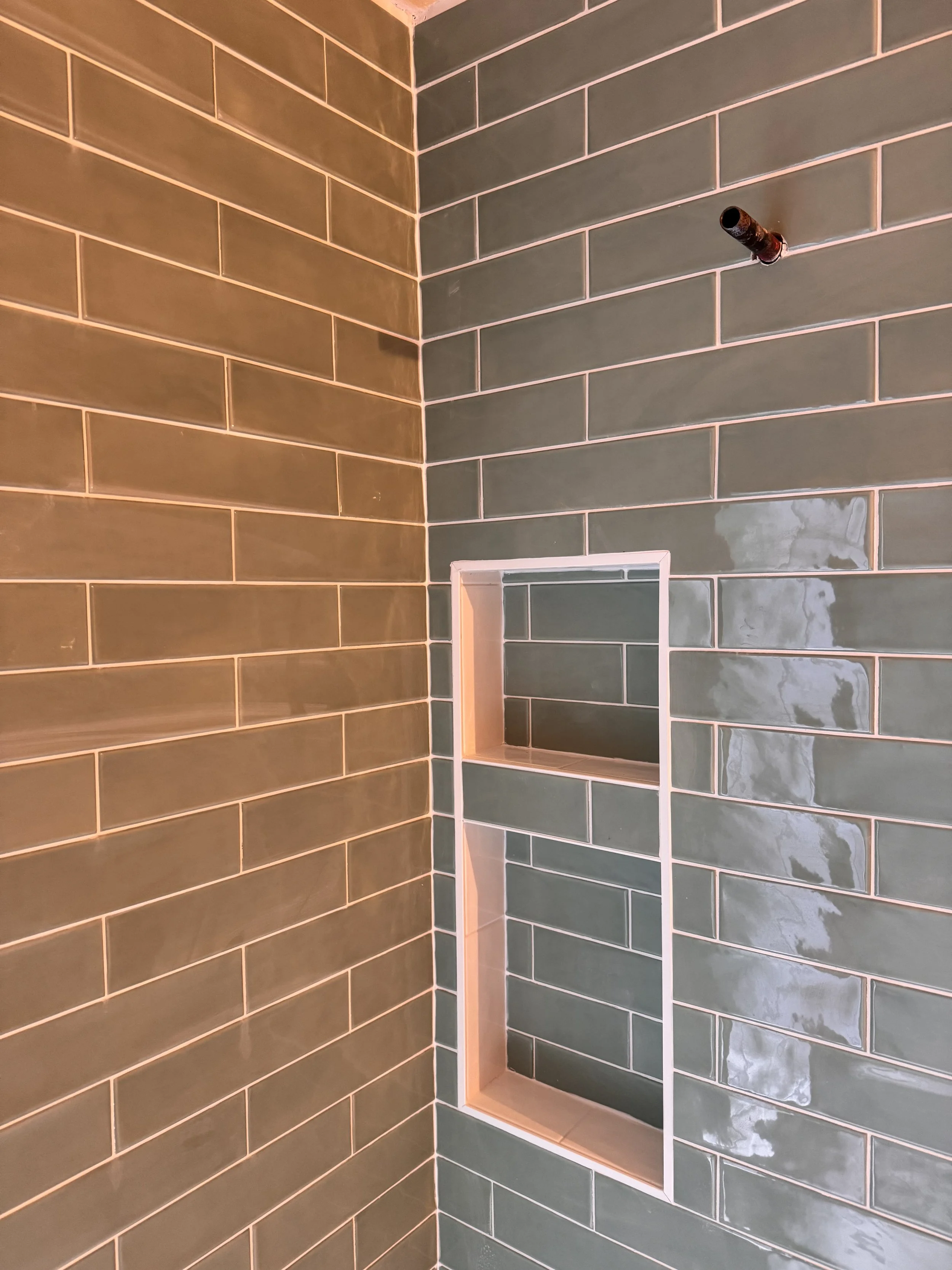 A partially constructed or renovated shower wall with green tiles and a built-in niche. The showerhead is missing, but the pipe is visible.
