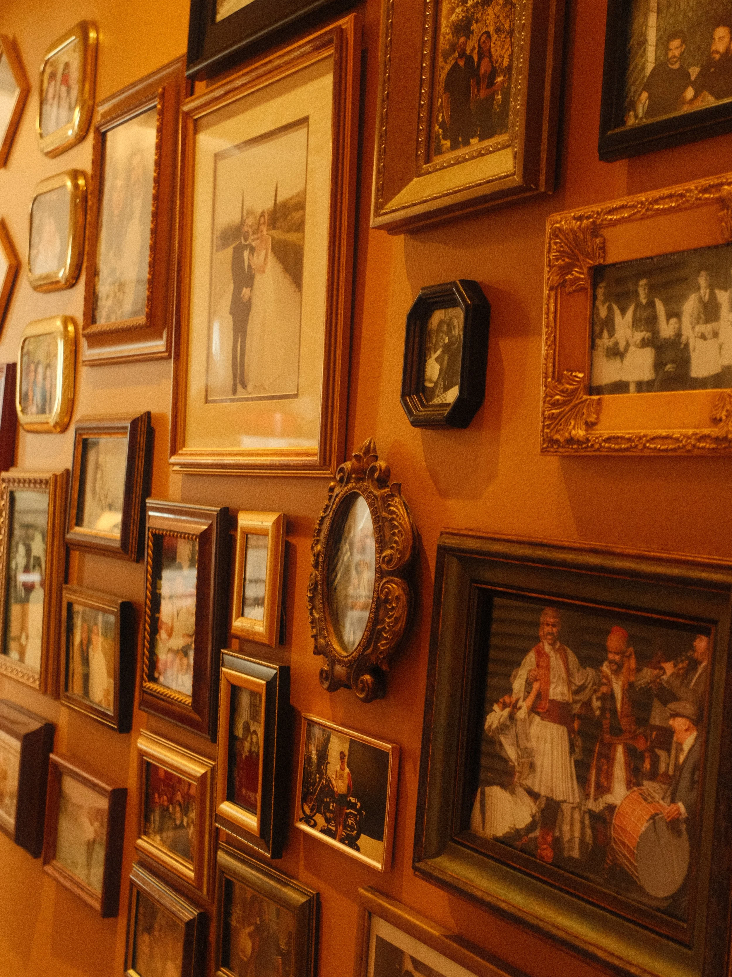 A wall decorated with multiple framed photographs and paintings, depicting various scenes including a couple in wedding attire, a group of people, and cultural performances.