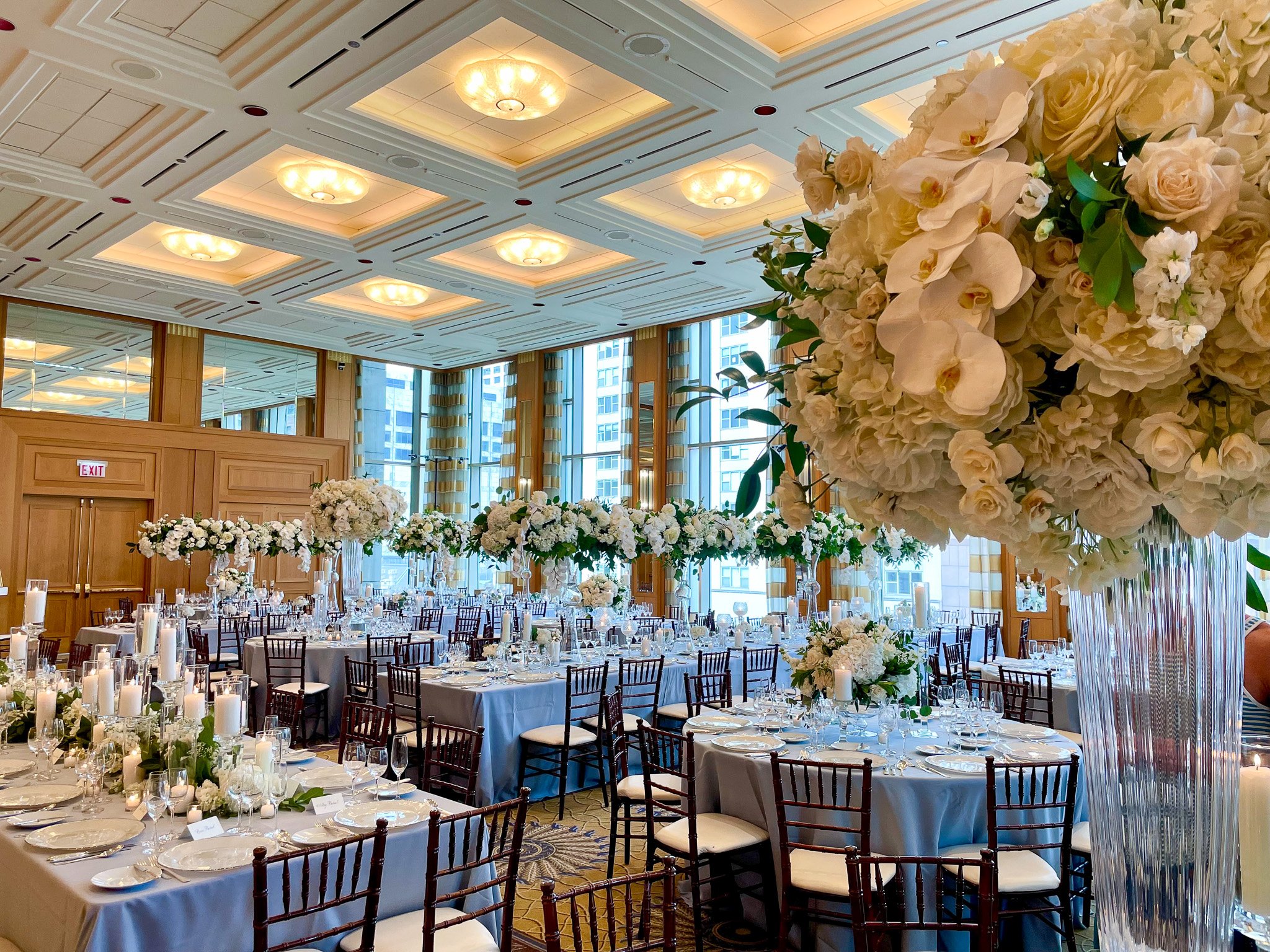 Elegant banquet hall decorated with white floral arrangements, candles, and chandeliers, set up for a wedding or formal event.