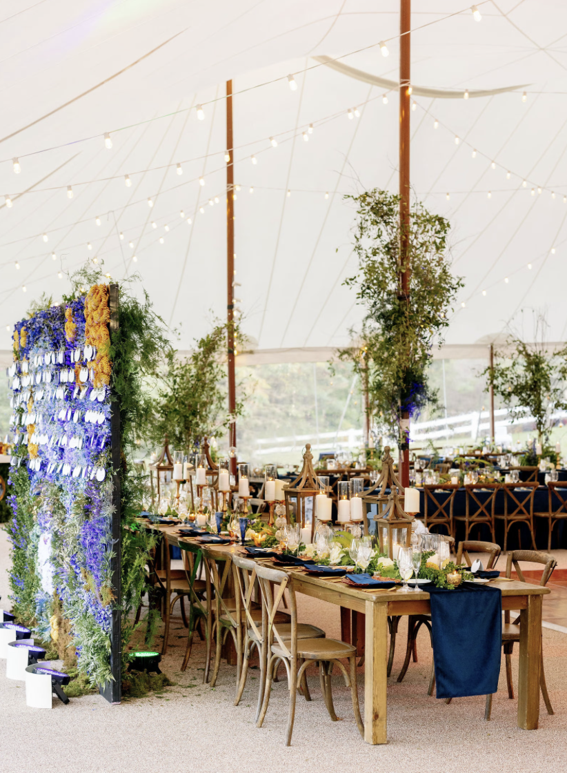 Decorated table setup inside a tent for a special event with string lights and greenery.