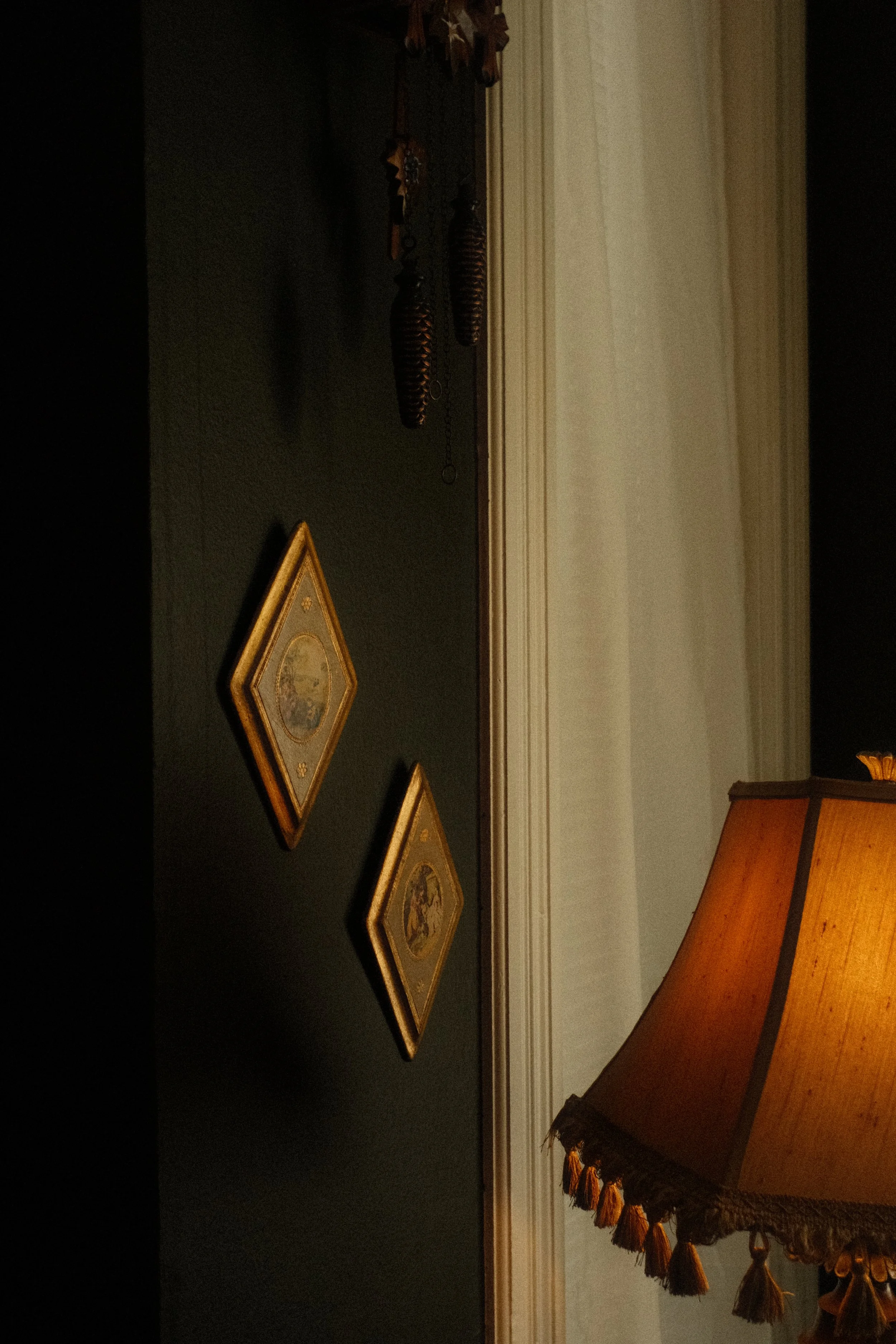 A dark-colored table with three triangular-shaped plaques or frames with gold-colored borders, and a corner of a fringed lampshade with tassels on the right side.