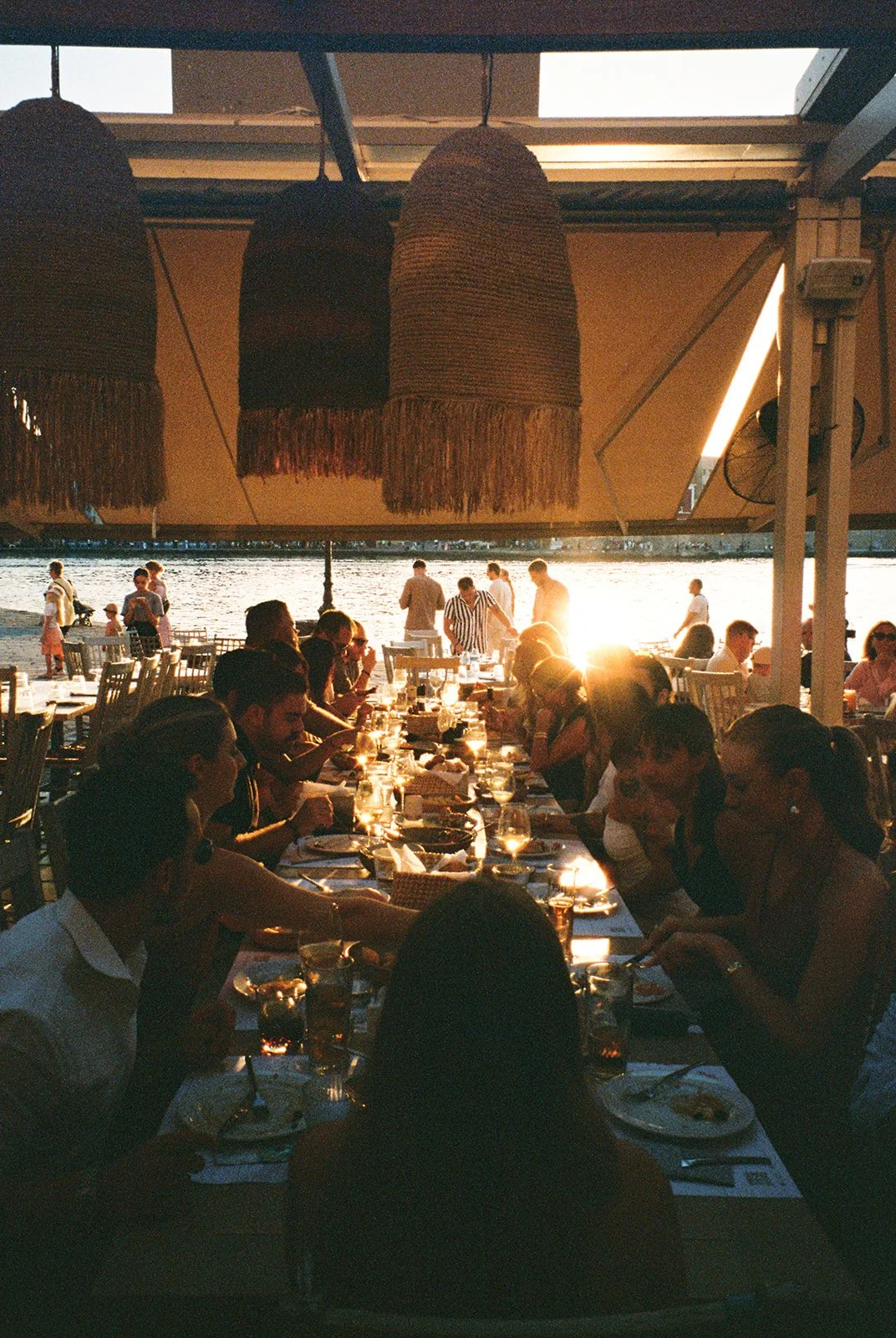 People dining at a waterfront restaurant during sunset.