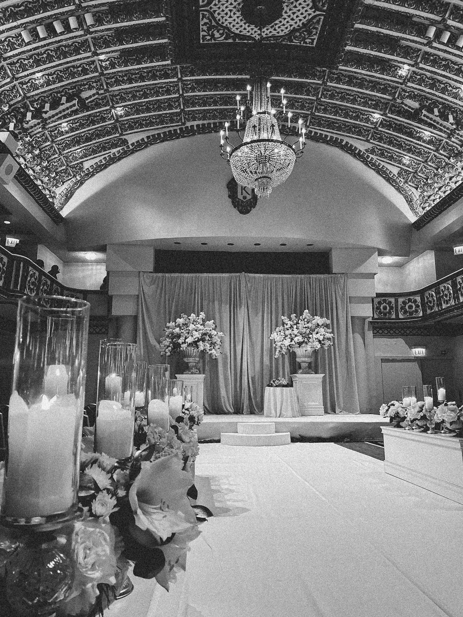 Interior of a decorated venue with a stage, floral arrangements, and draped curtains, suggesting a wedding or special event setup.