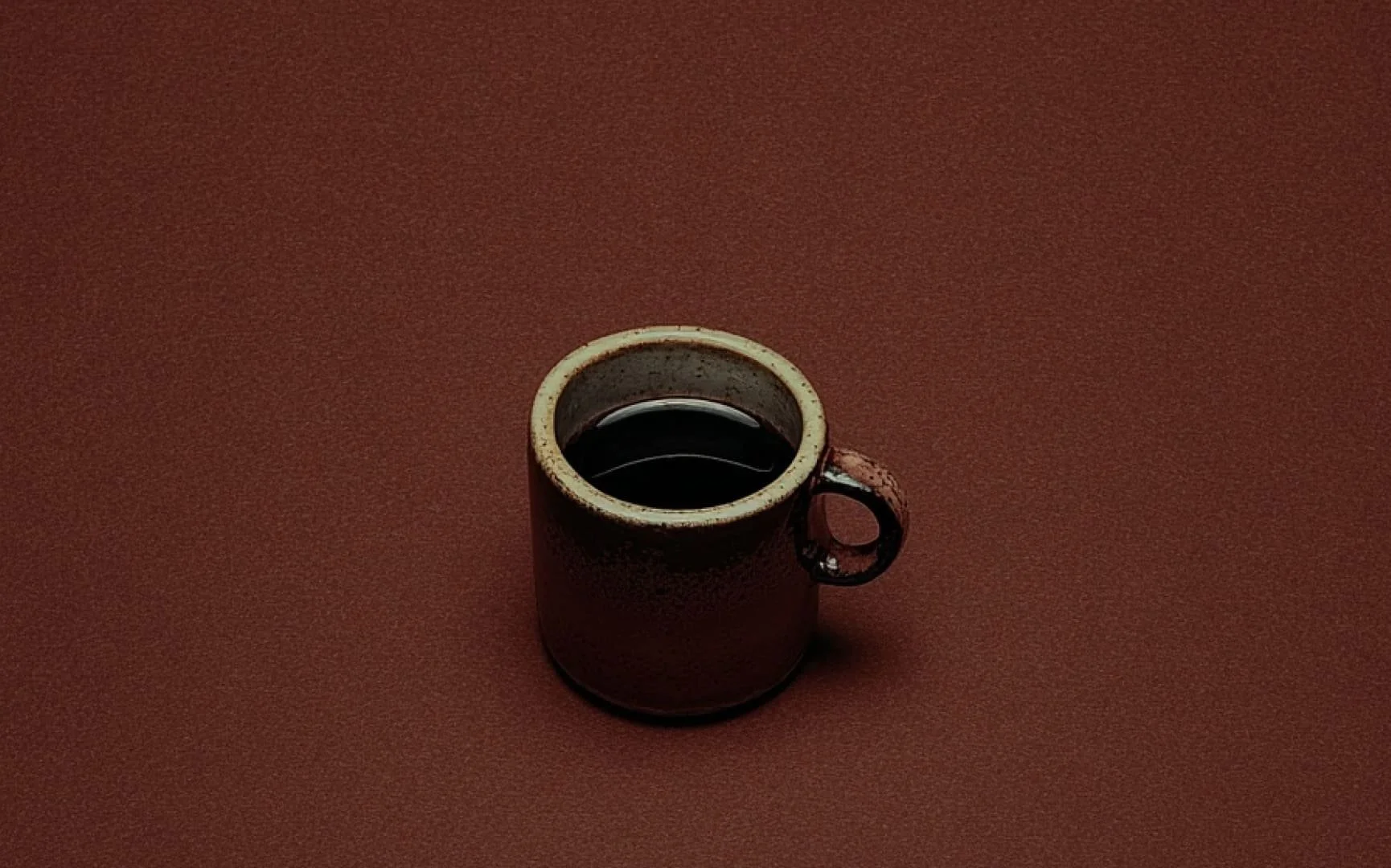 A ceramic mug filled with black coffee on a red textured surface.