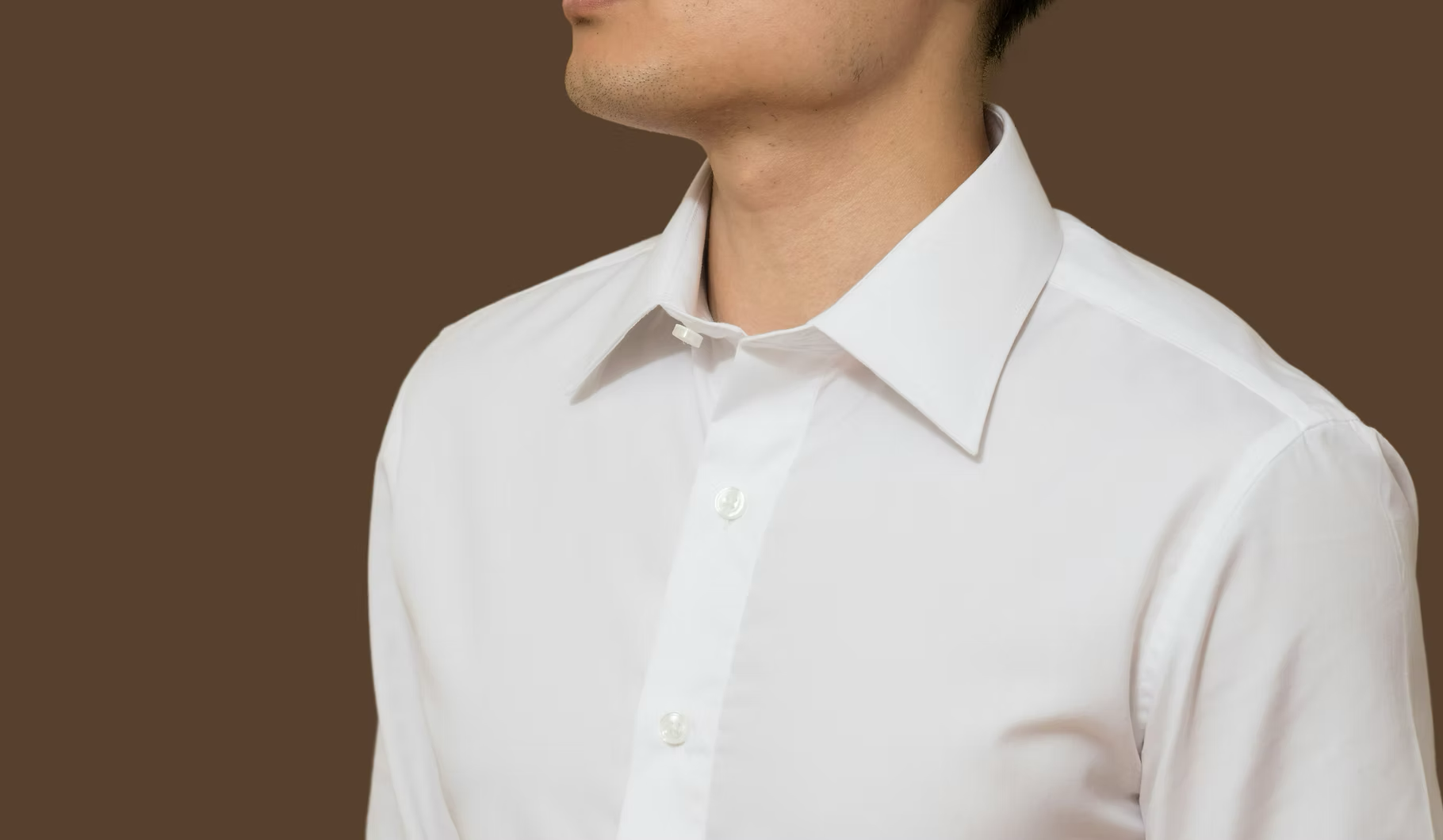 Close-up of a man wearing a white dress shirt against a brown background, showing the collar and upper chest.