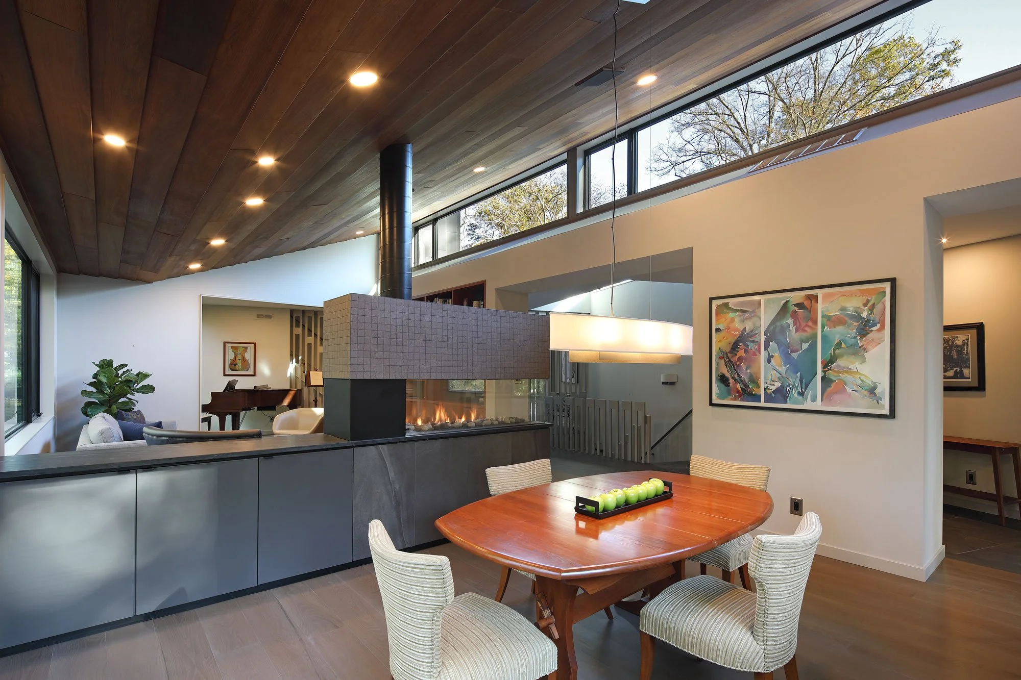 Open living and dining space at Hadro House Haddonfield NJ — salvaged mahogany ceiling, clerestory windows, and three-sided gas fireplace dividing the rooms without walls