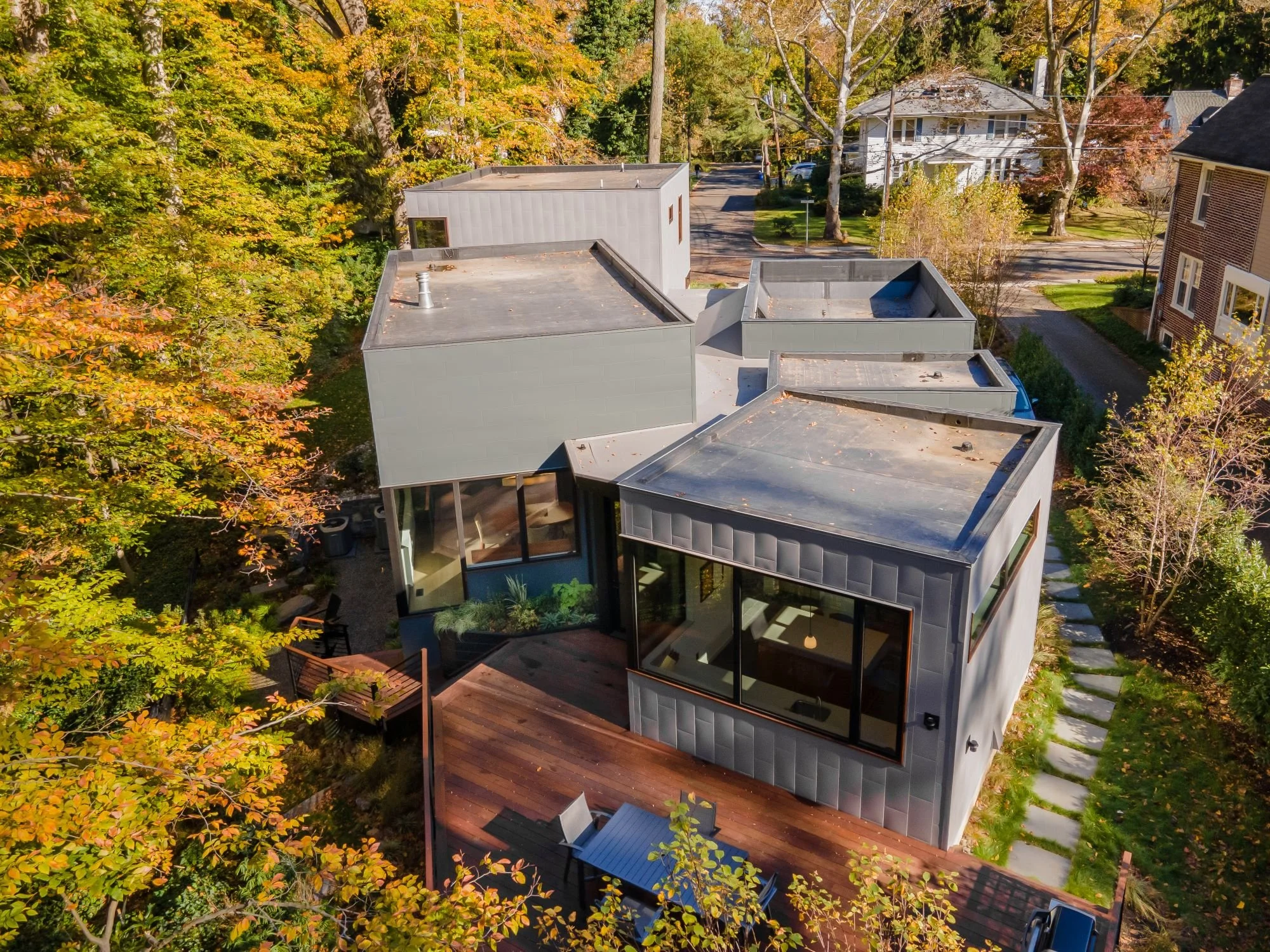 Aerial drone photo of Hadro House in Haddonfield NJ showing discrete cubic volumes with flat roofs scattered across a wooded sloping site above a stream, contemporary home among traditional neighbors