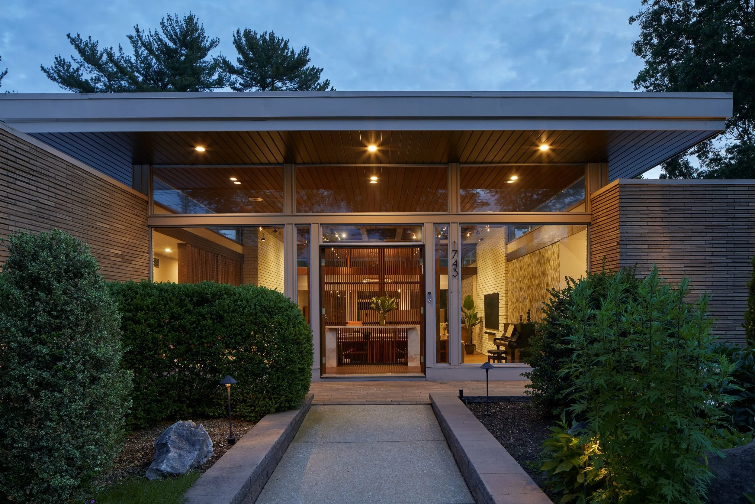Renovated 1964 mid-century modern home in Cherry Hill, NJ with glass front entry, floating roof plane, oak slat screen, landscape lighting, and horizontal masonry.