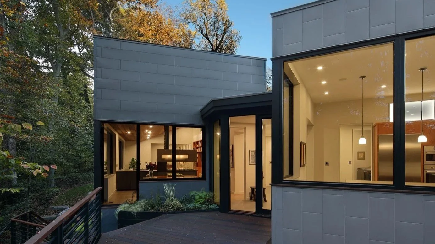 Modern custom home in Haddonfield, NJ with large glass openings connecting interior living spaces to a wooded streamside deck.