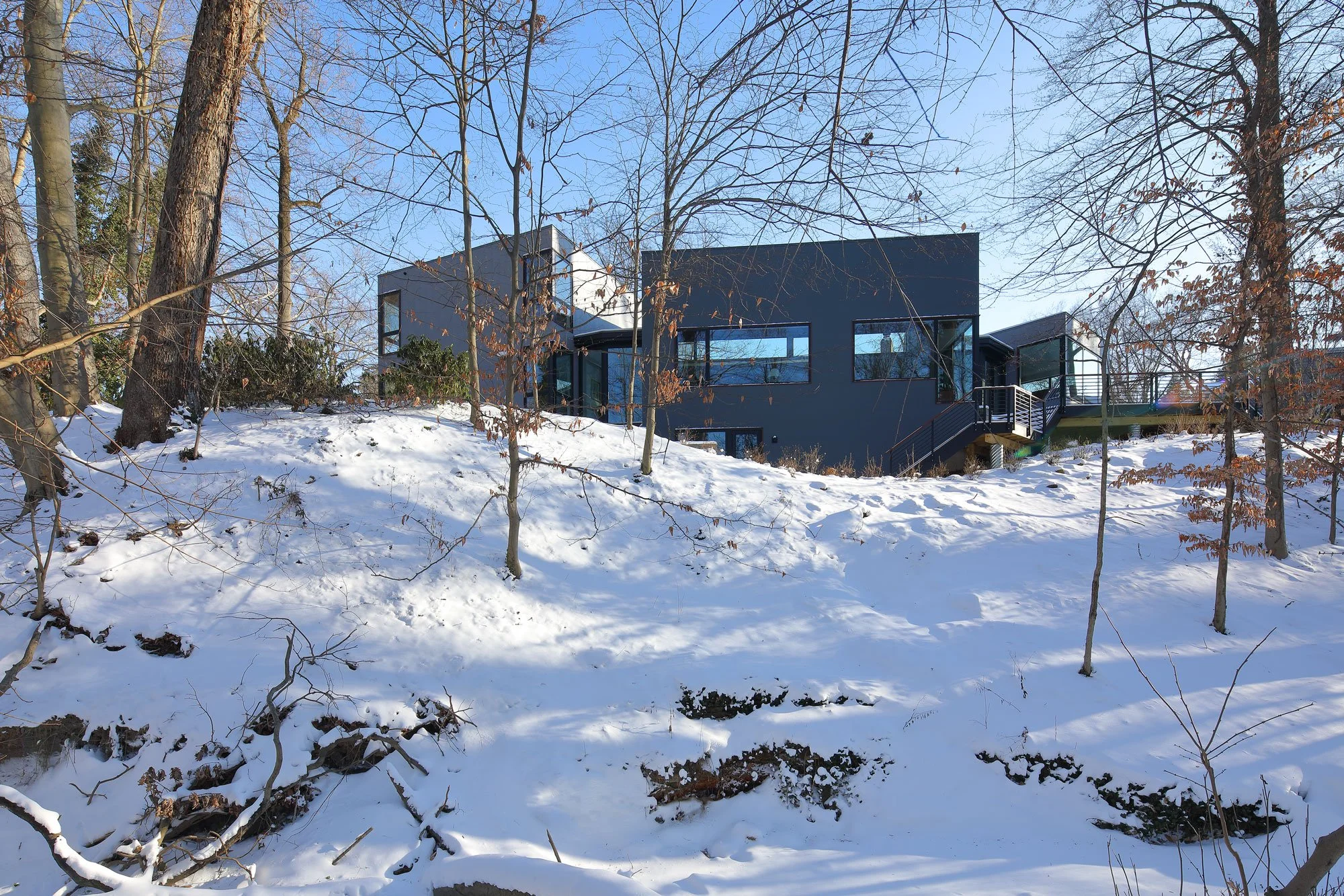 Hadro House in Haddonfield NJ in its first winter — dark steel-clad volumes with glowing windows above the snow-covered stream ravine