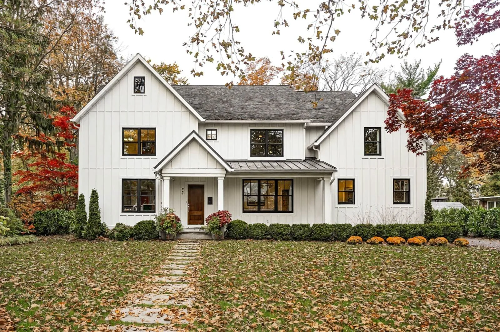 White House Black Windows Shadow custom new home Haddonfield NJ — white board and batten siding black fiberglass windows standing seam metal entry porch roof warm wood front door autumn landscaping J Reinert Architecture