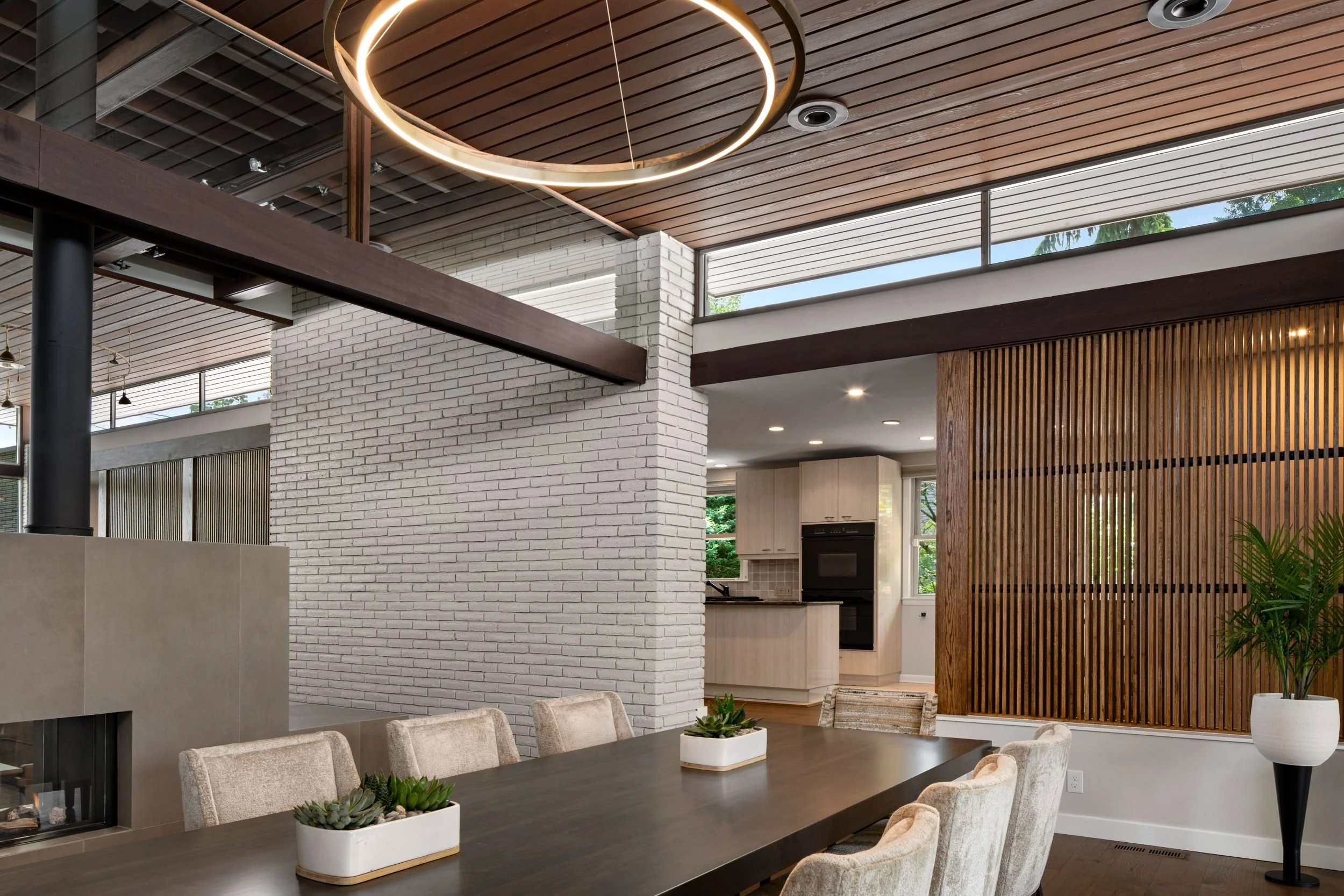 Renovated mid-century modern dining room looking toward kitchen Cherry Hill NJ — floating fireplace white brick structural wall oak slat screen kitchen connection open plan clerestory windows wood ceiling J Reinert Architecture