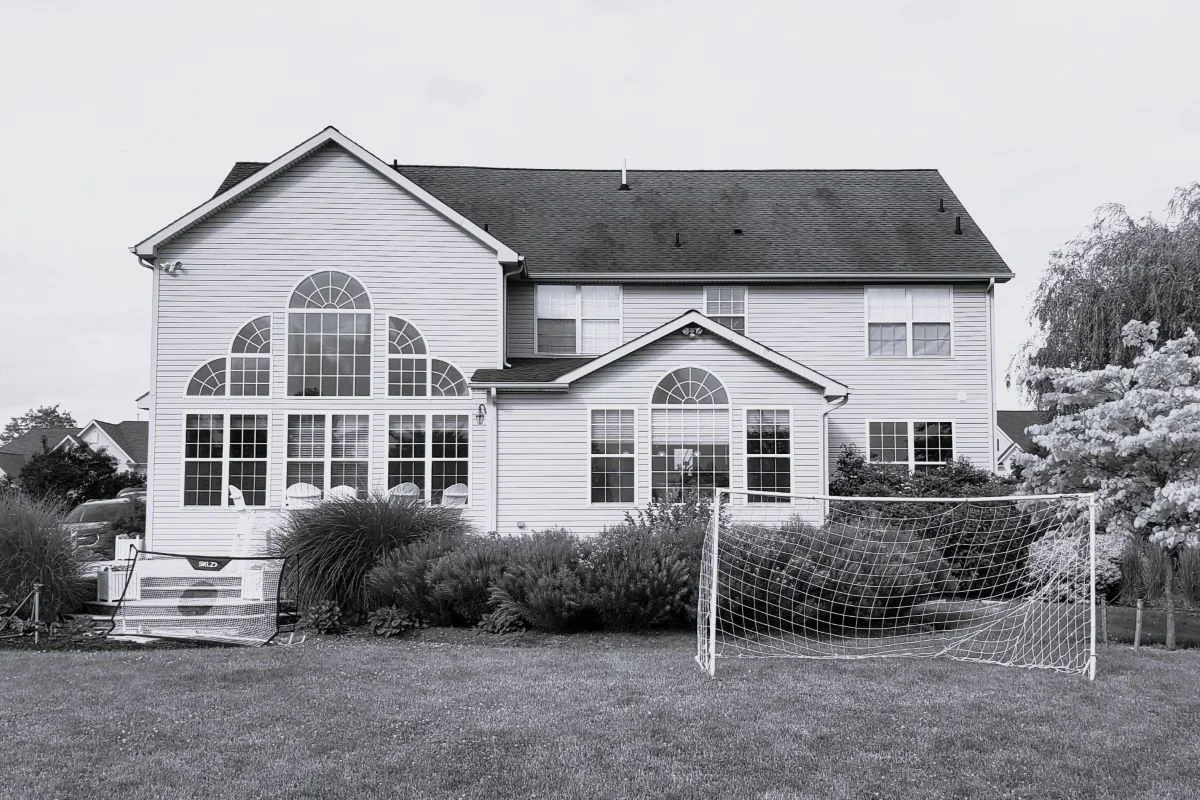 Before photo of the rear elevation of a 1990s developer home in Mullica Hill, New Jersey, showing arched windows and the original double-height living room before renovation.