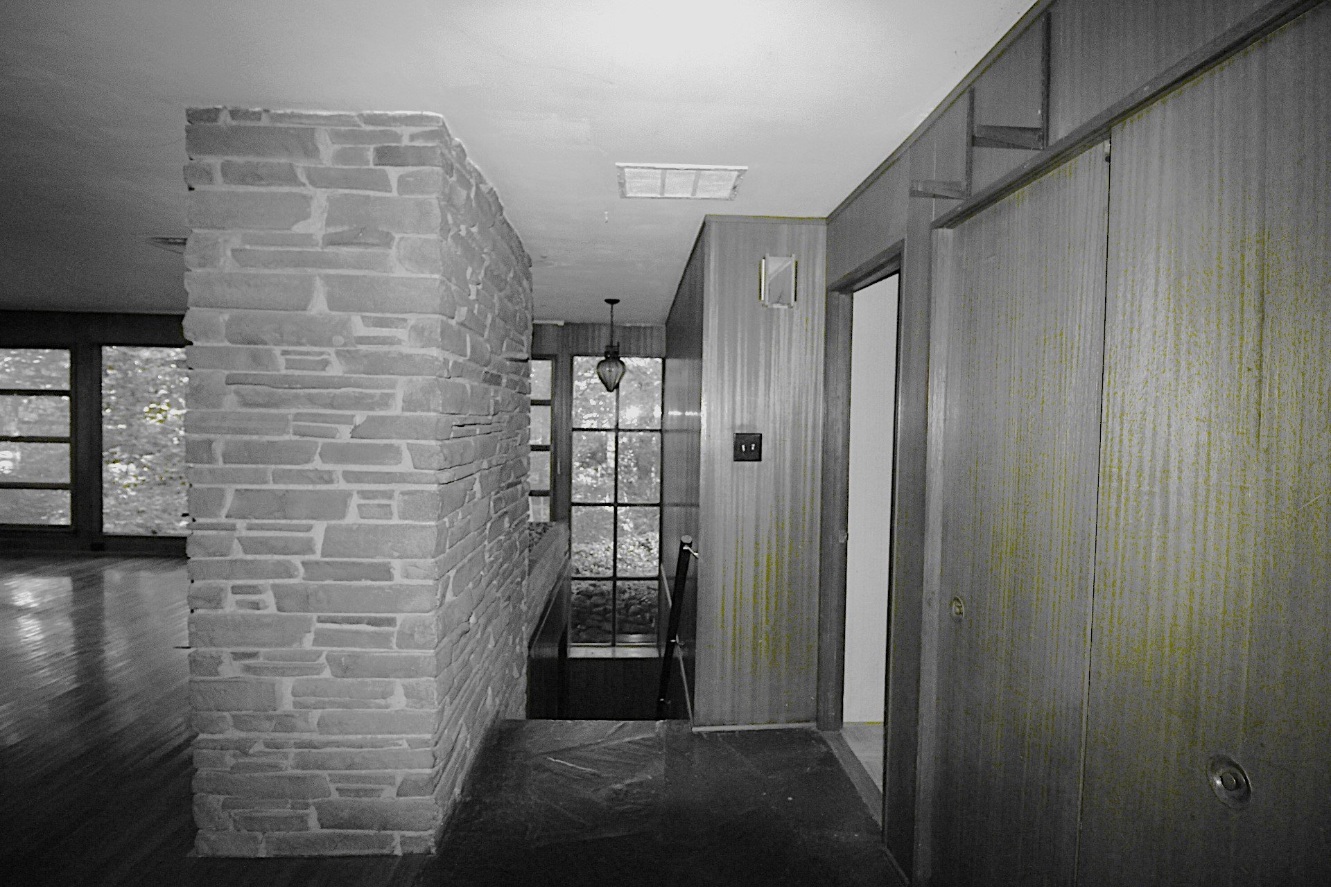 Entry hall of the original 1948 mid-century home on the Hadro House site in Haddonfield NJ — stacked stone wall, wood paneling, and window to the woods, photographed before demolition