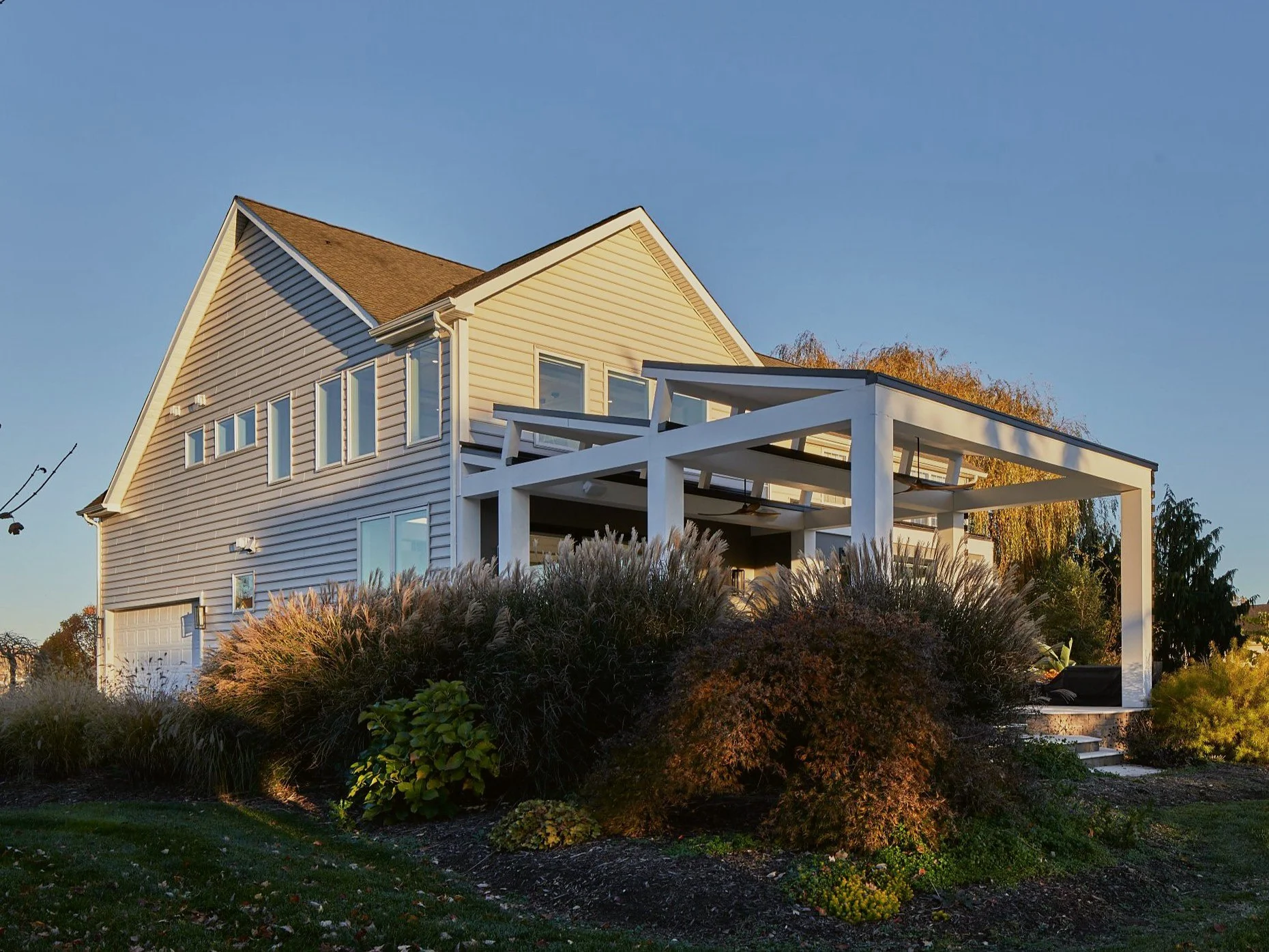 Golden-hour side view of a renovated 1990s home in Mullica Hill, NJ, with a new white post-and-beam pergola over a covered outdoor living area.