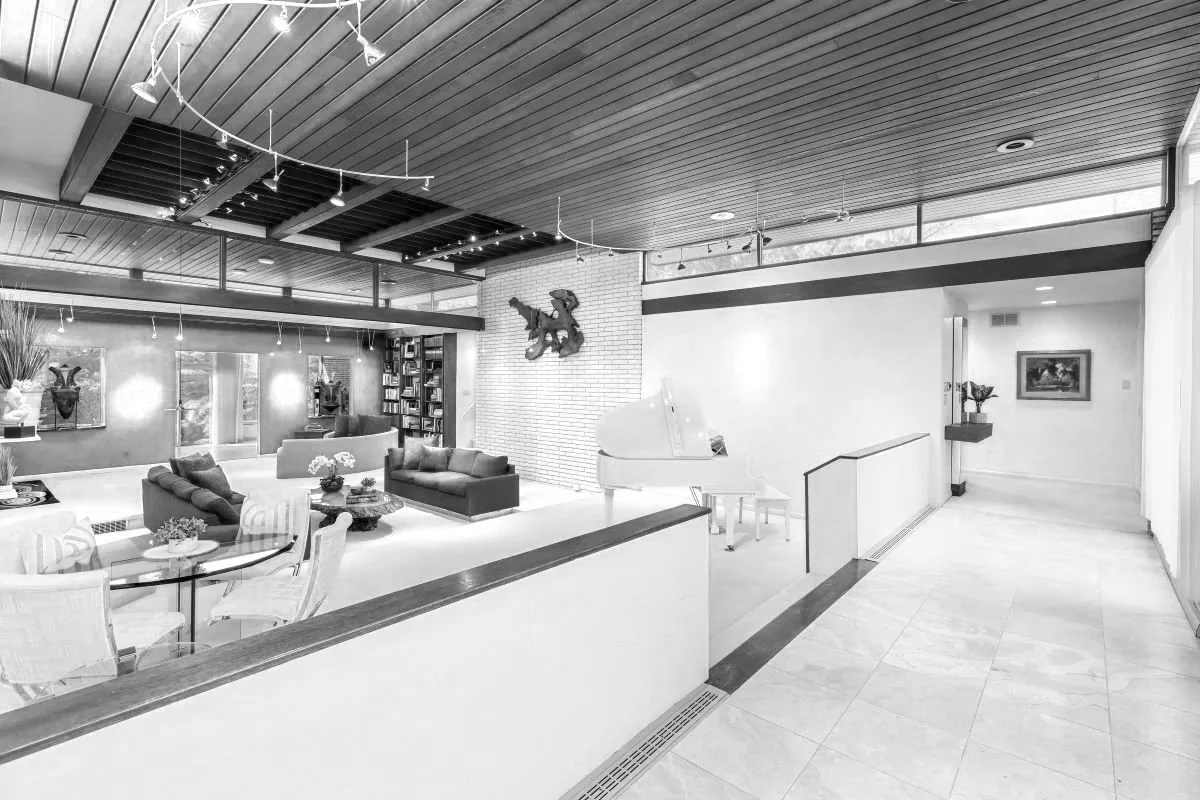 Before photo of the open living room in a Cherry Hill, NJ mid-century modern home, showing clerestory windows, wood ceiling, white brick wall, and open interior volume before renovation.