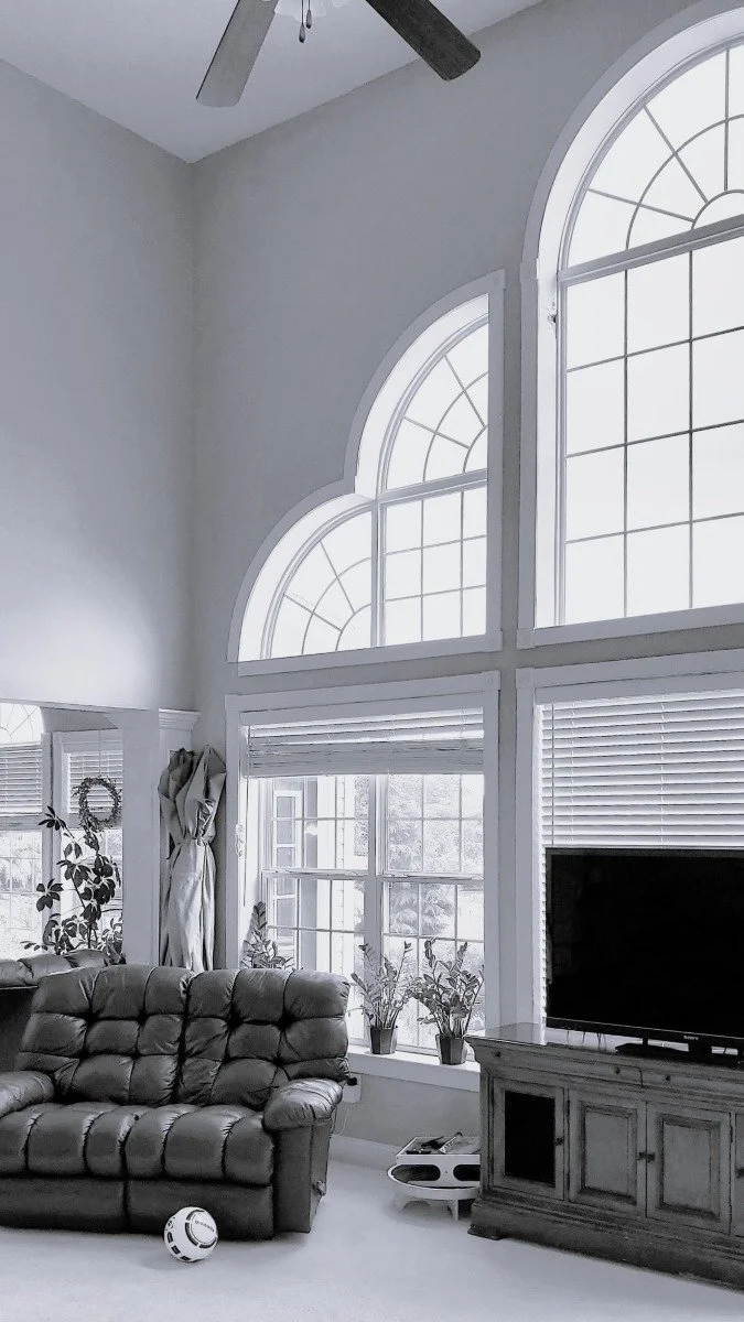 Before photo of a double-height living room in a 1990s developer home in Mullica Hill, New Jersey, showing arched windows and oversized interior volume before renovation.