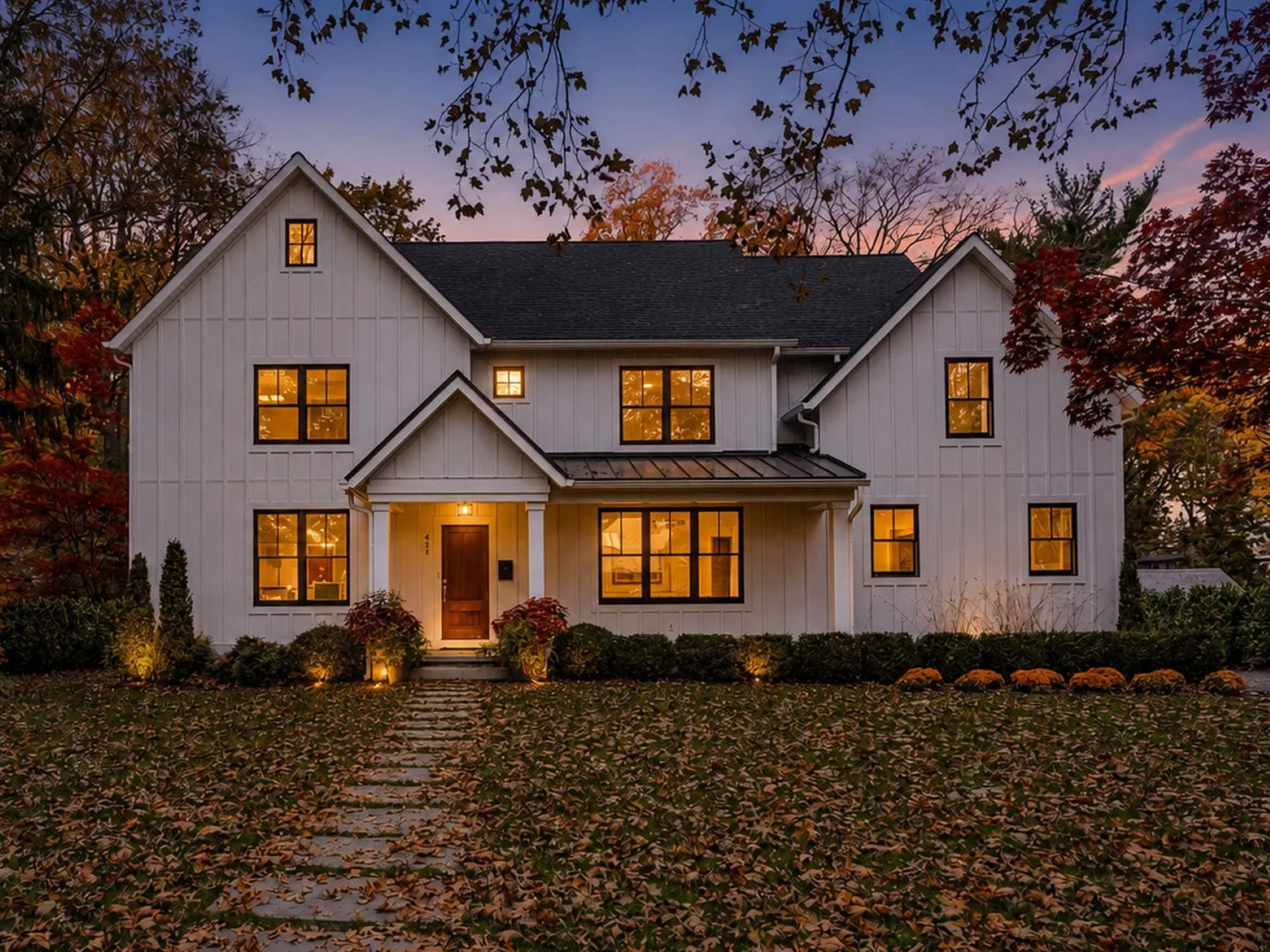 Twilight front elevation of a new white board-and-batten modern farmhouse with black windows and a gabled entry porch, Haddonfield, NJ.