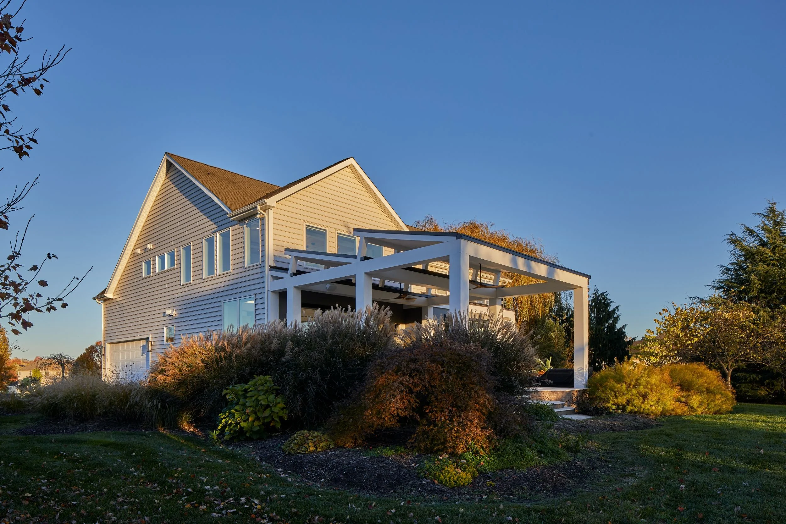 Rear three-quarter view of a 1990s developer home in Mullica Hill NJ transformed by J Reinert Architecture, with a white structural grid and open pergola extending from the original gable-end volume at golden hour
