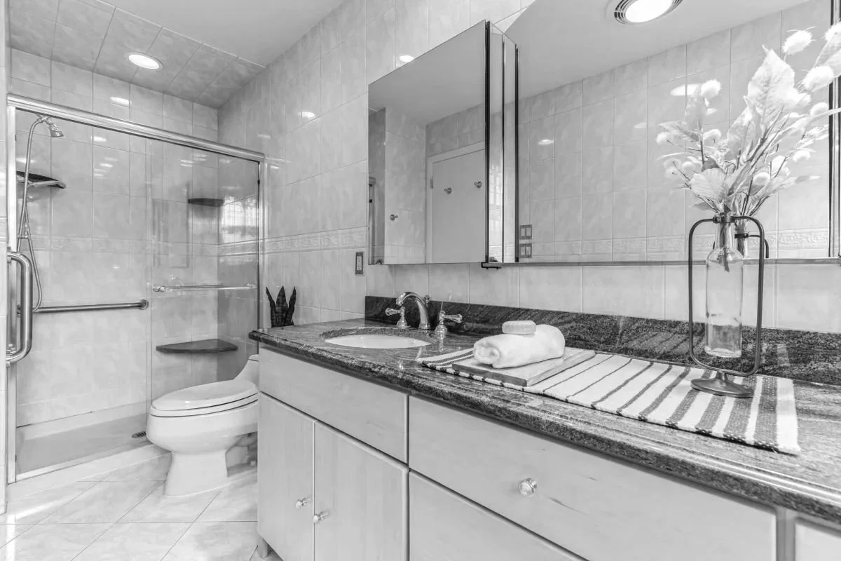 Before photo of a primary bathroom in a Cherry Hill, NJ mid-century modern home before renovation, showing dated tile, vanity, mirrors, and shower enclosure.