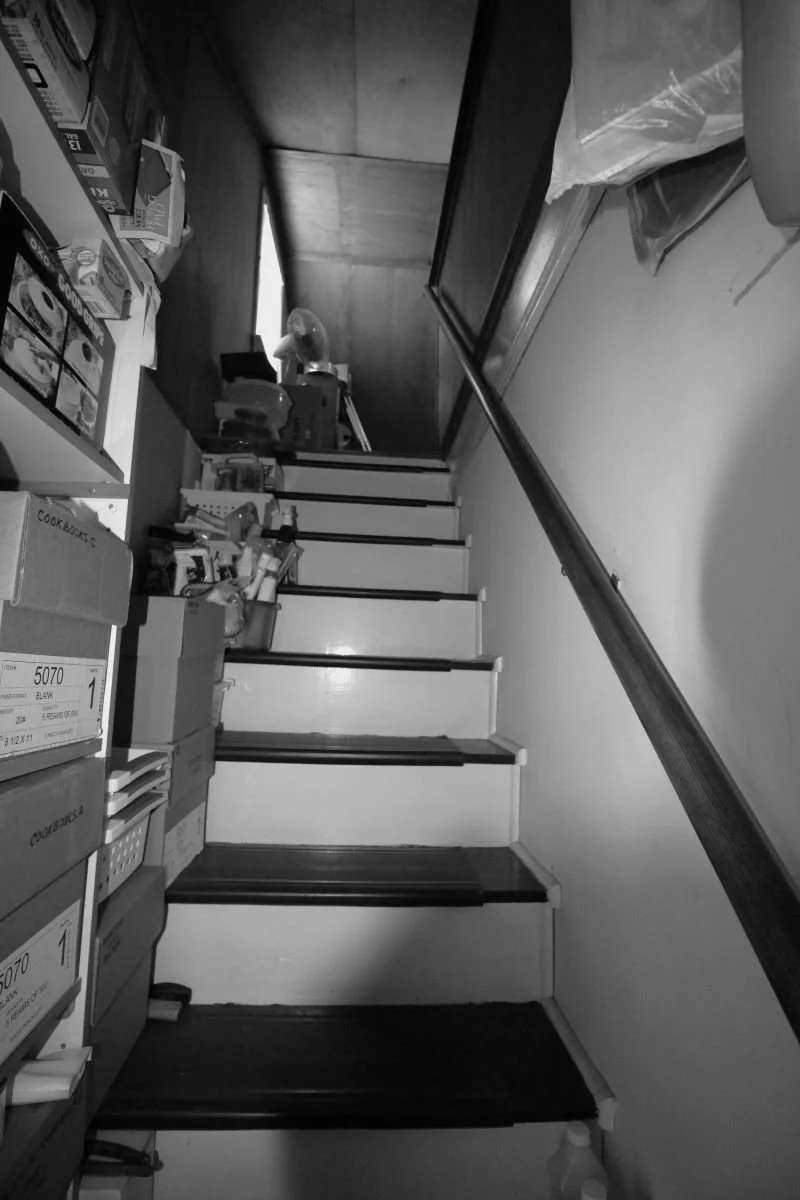 Before renovation — steep dark stair ascending to unfinished attic storage at cape cod home in Haddon Heights NJ with boxes stacked along walls, prior to J Reinert Architecture renovation