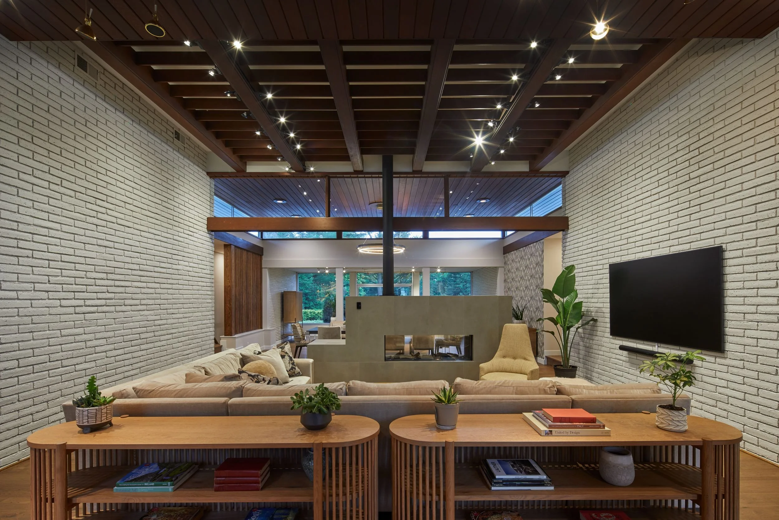 Renovated mid-century modern living room Cherry Hill NJ — white brick walls both sides floating two-sided fireplace centered rear glazing garden views structural ceiling expressed full central volume symmetry J Reinert Architecture