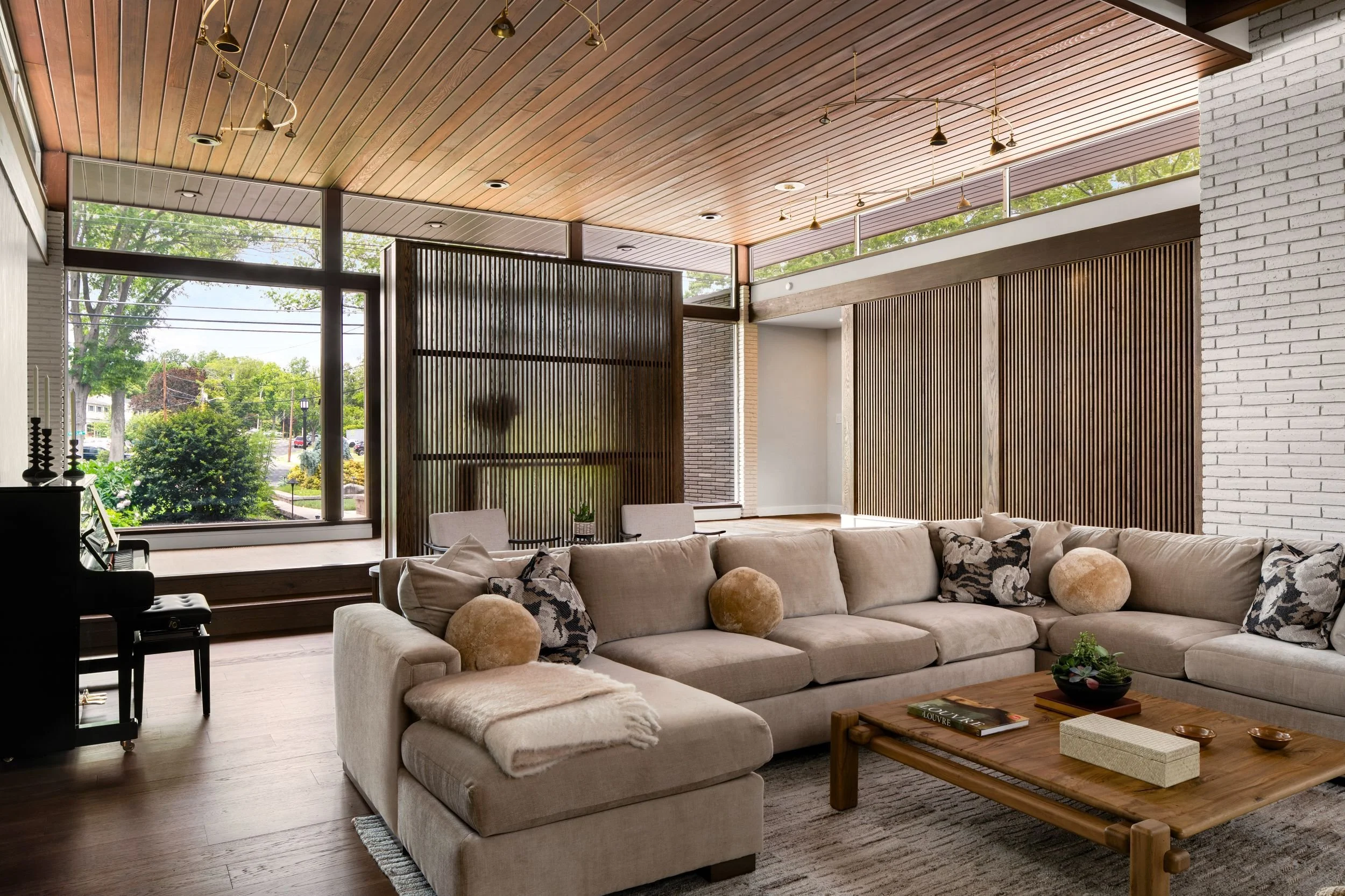 Renovated mid-century modern family room in Cherry Hill, NJ with oak slat screen walls, clerestory windows, wood ceiling, white brick, piano, and open seating area.