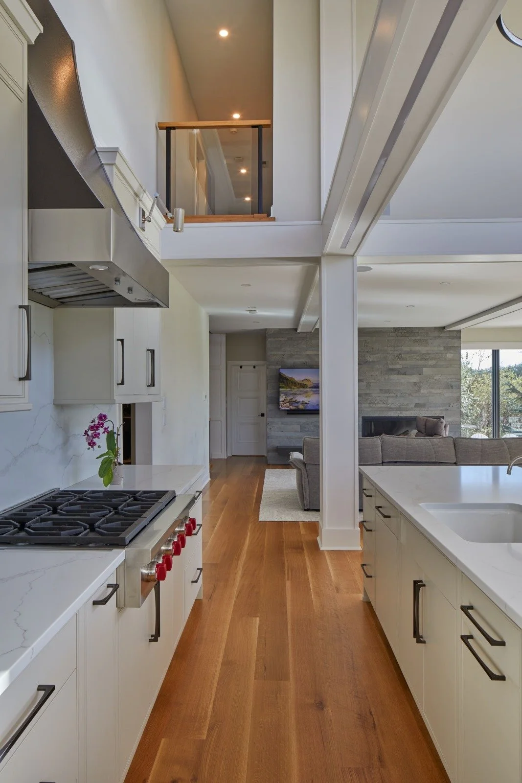 Renovated kitchen in a Mullica Hill, New Jersey home with white cabinetry, white oak floors, structural columns, and a view into the family room beyond.